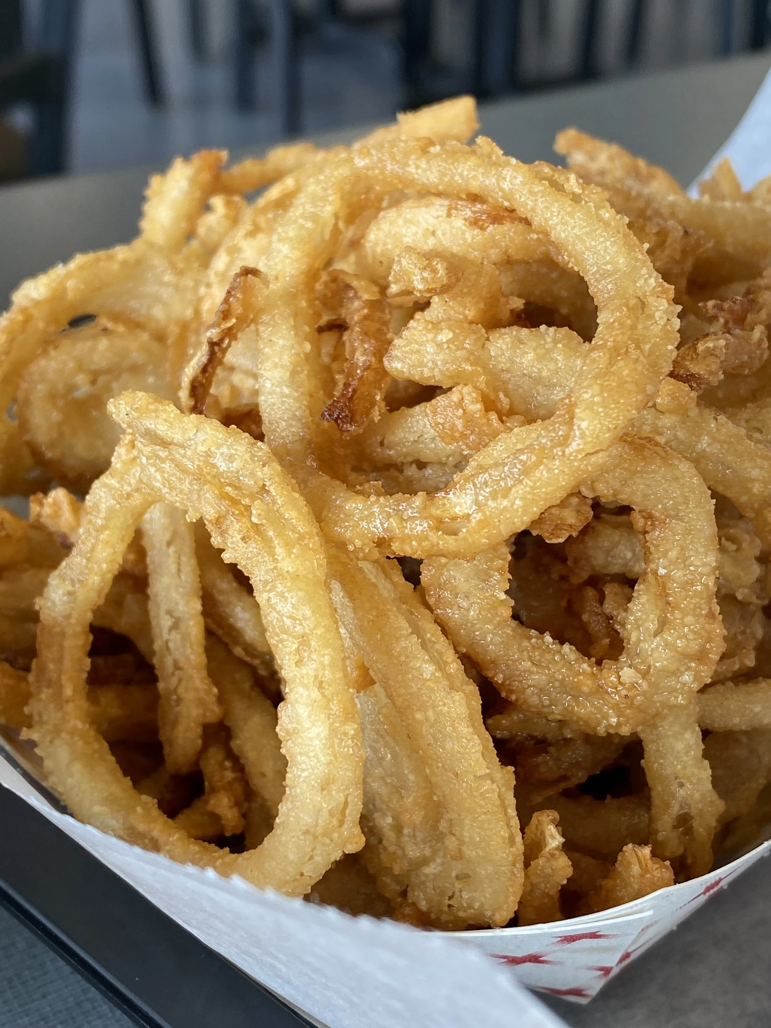 A close-up of a serving of crispy, golden fried onion rings in a paper food boat.