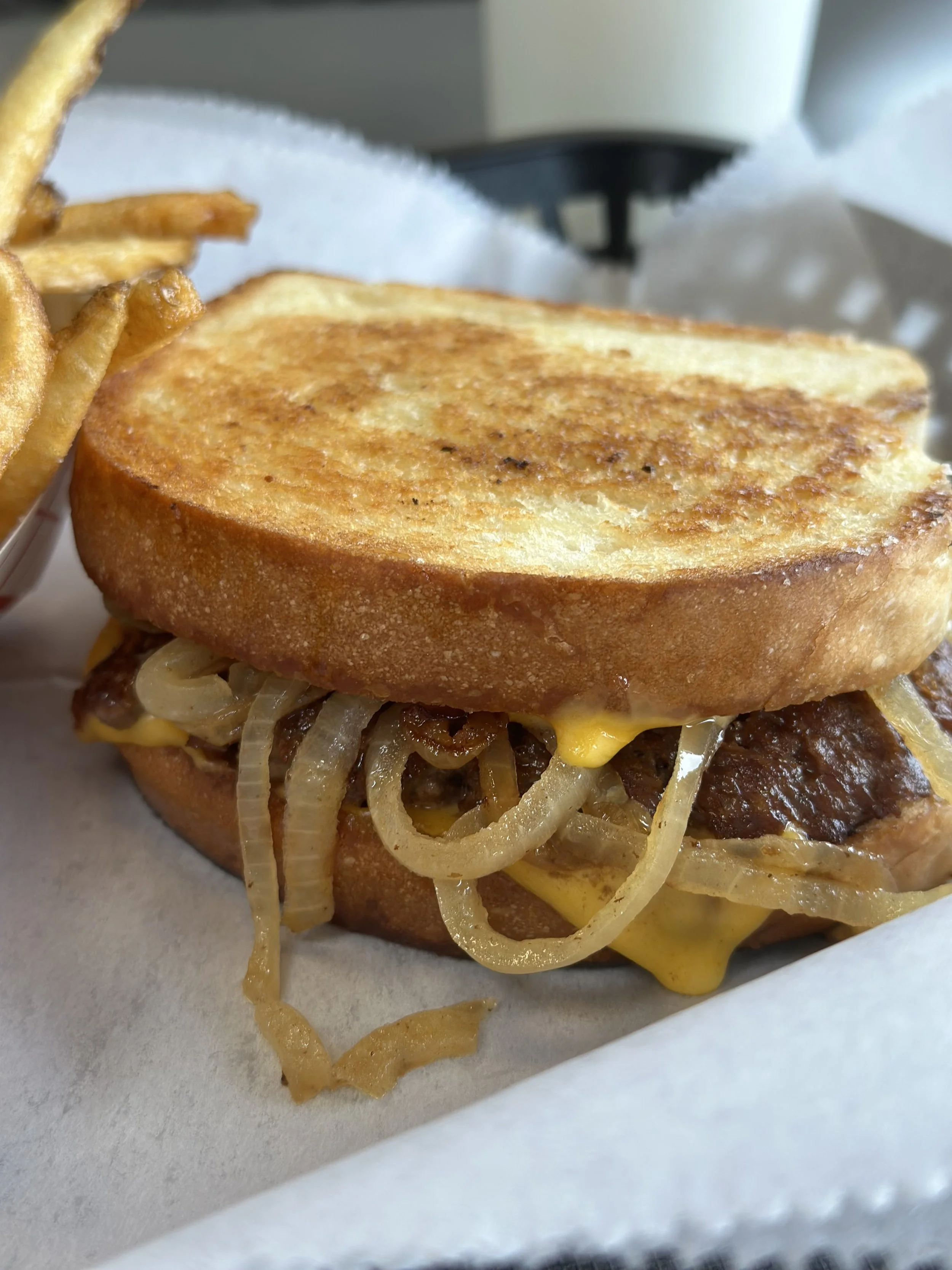 Close-up of a grilled cheese sandwich with caramelized onions inside, served with a side of French fries.