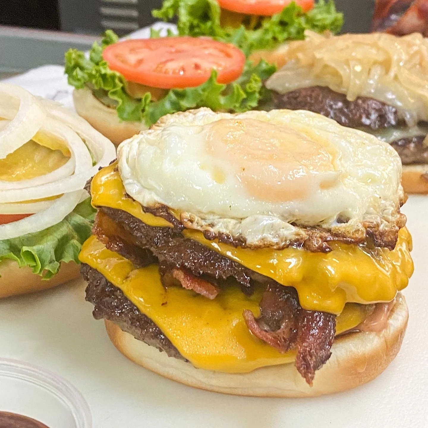 Close-up of a breakfast burger with bacon, cheddar cheese, a fried egg, and a toasted bun, served with a side of onion, tomato, and lettuce salad.