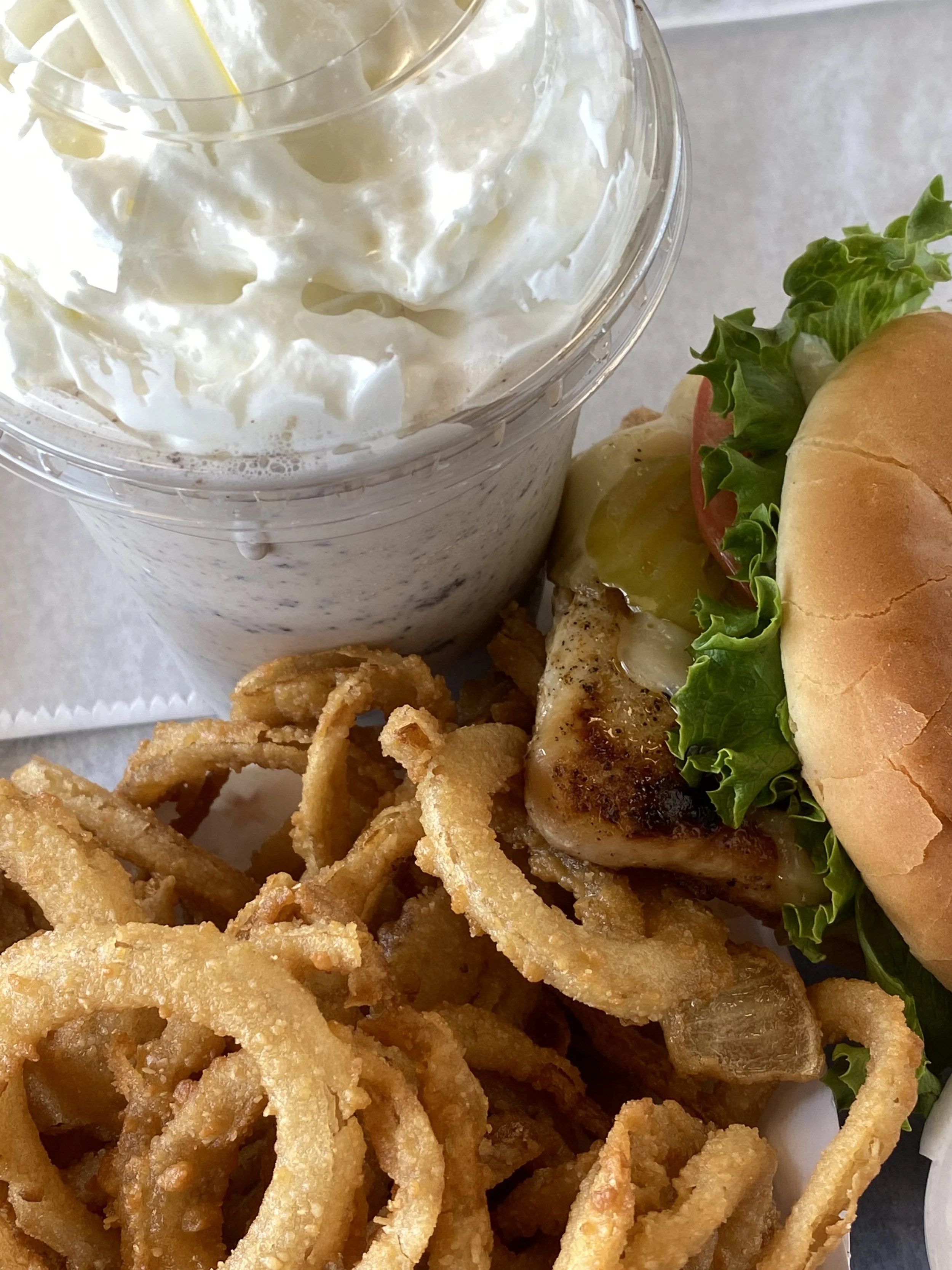 A fast food meal with fried calamari, a cheeseburger with lettuce, tomato, and pickles, and a milkshake topped with whipped cream.