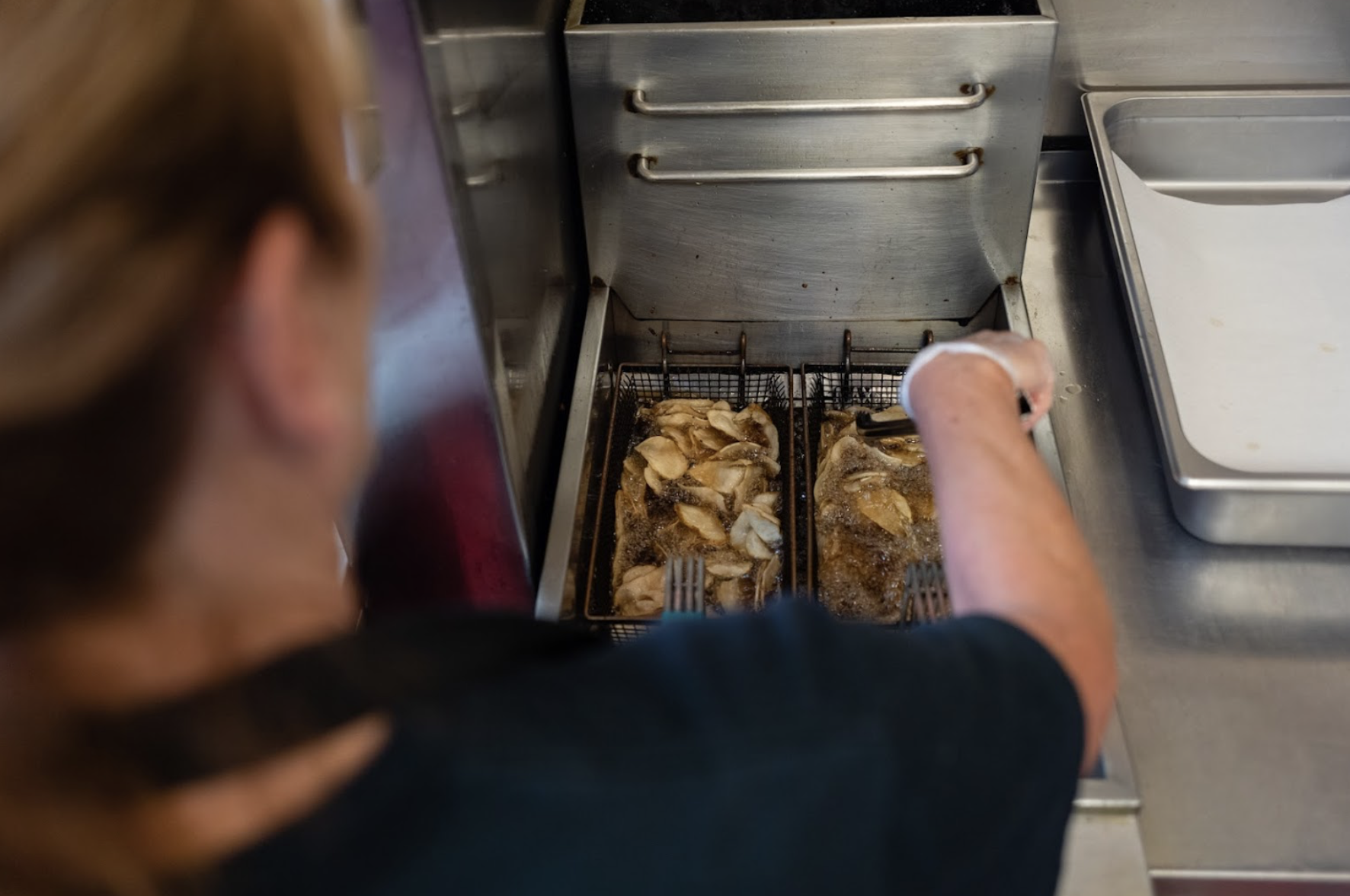 A person cooking chicken wings in a deep fryer at a restaurant kitchen.