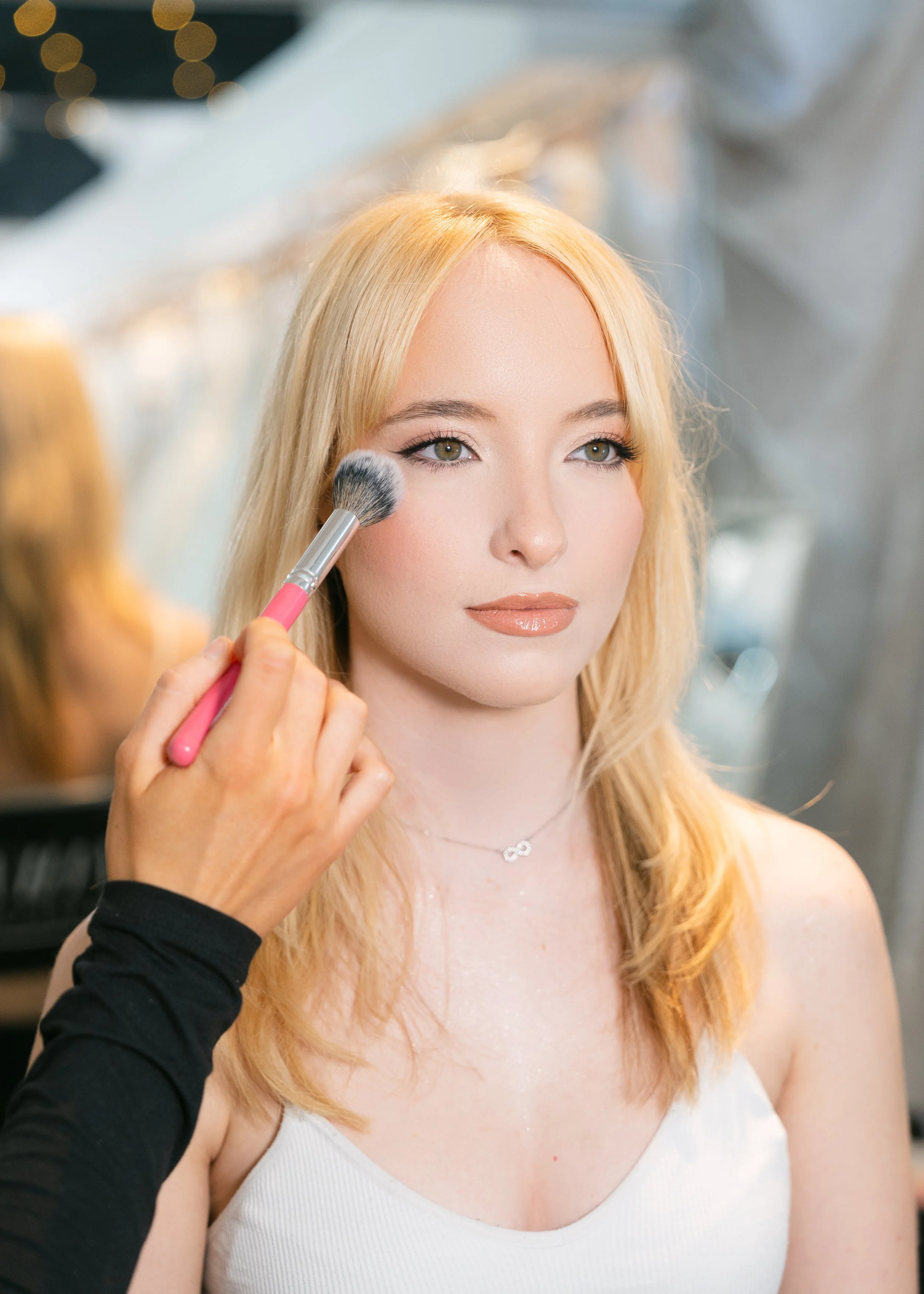 a blonde women getting her makeup done applying blush to face