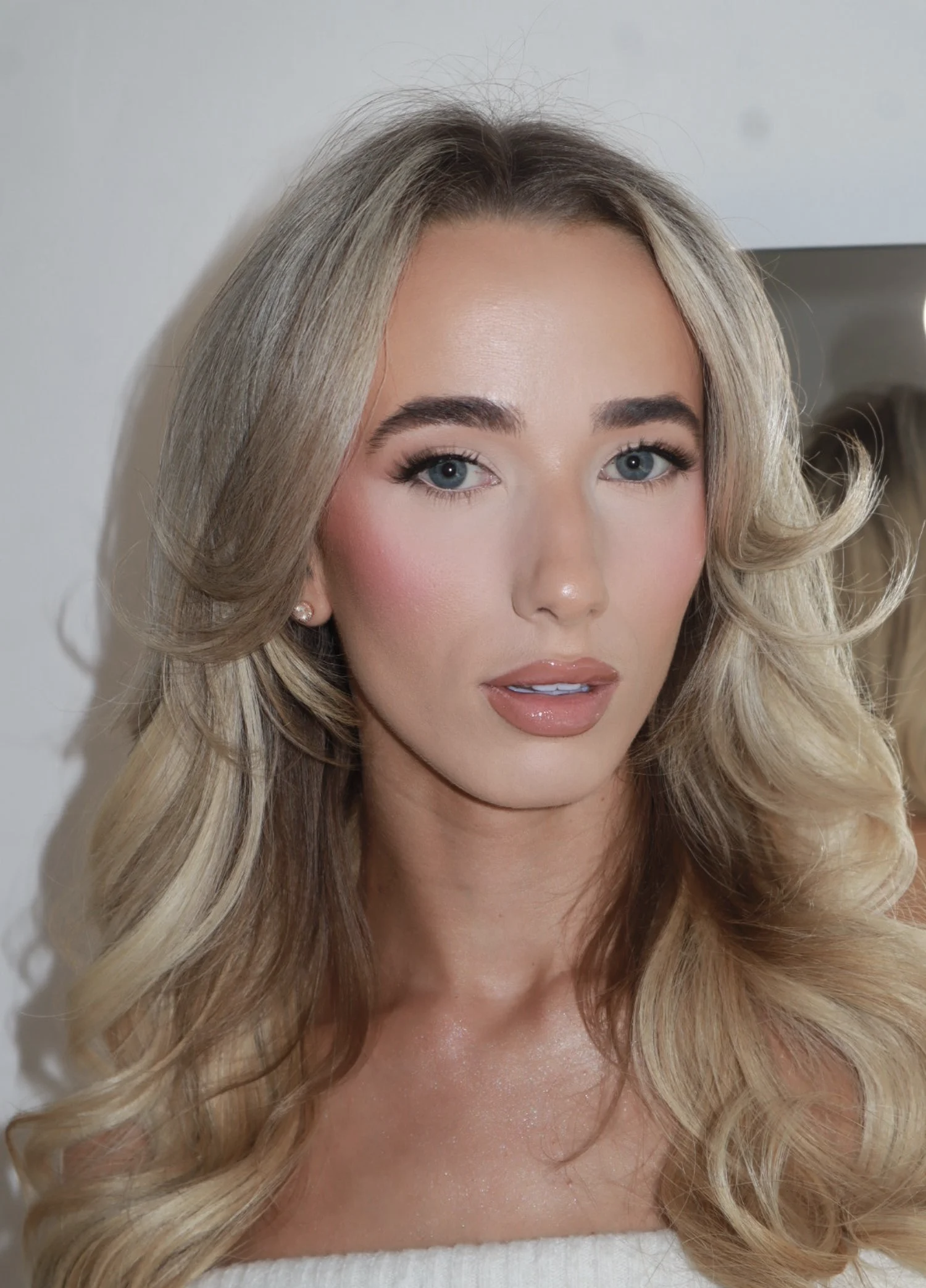 Close-up of a woman with blonde, wavy hair and light makeup, looking directly at the camera.