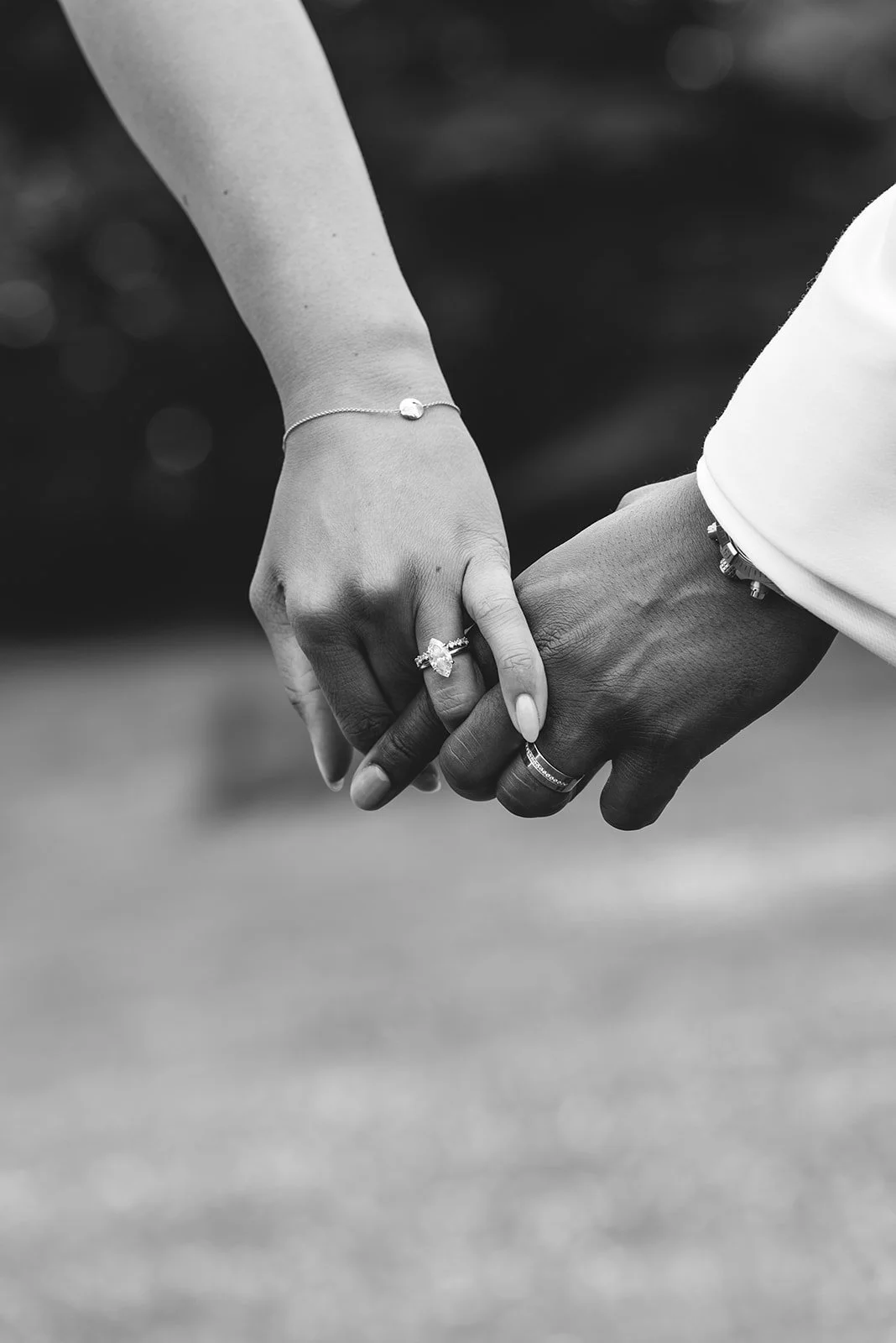 Close-up of a couple holding hands, showing wedding rings and jewelry, black and white photograph.