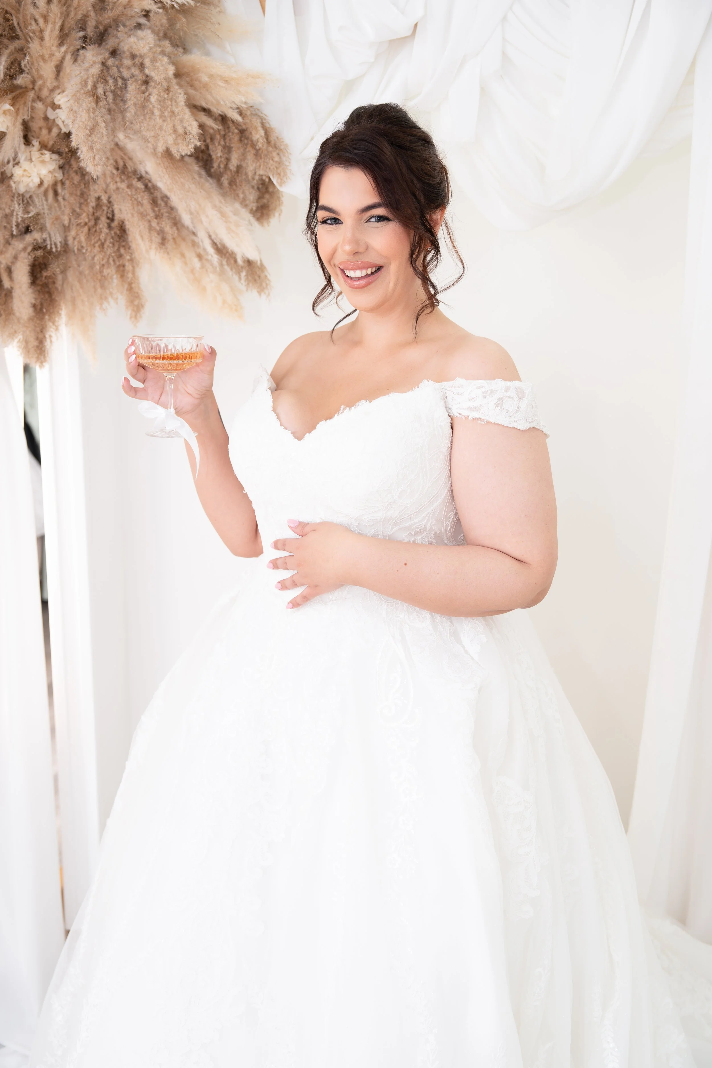A smiling bride in a white wedding dress holding a champagne glass.