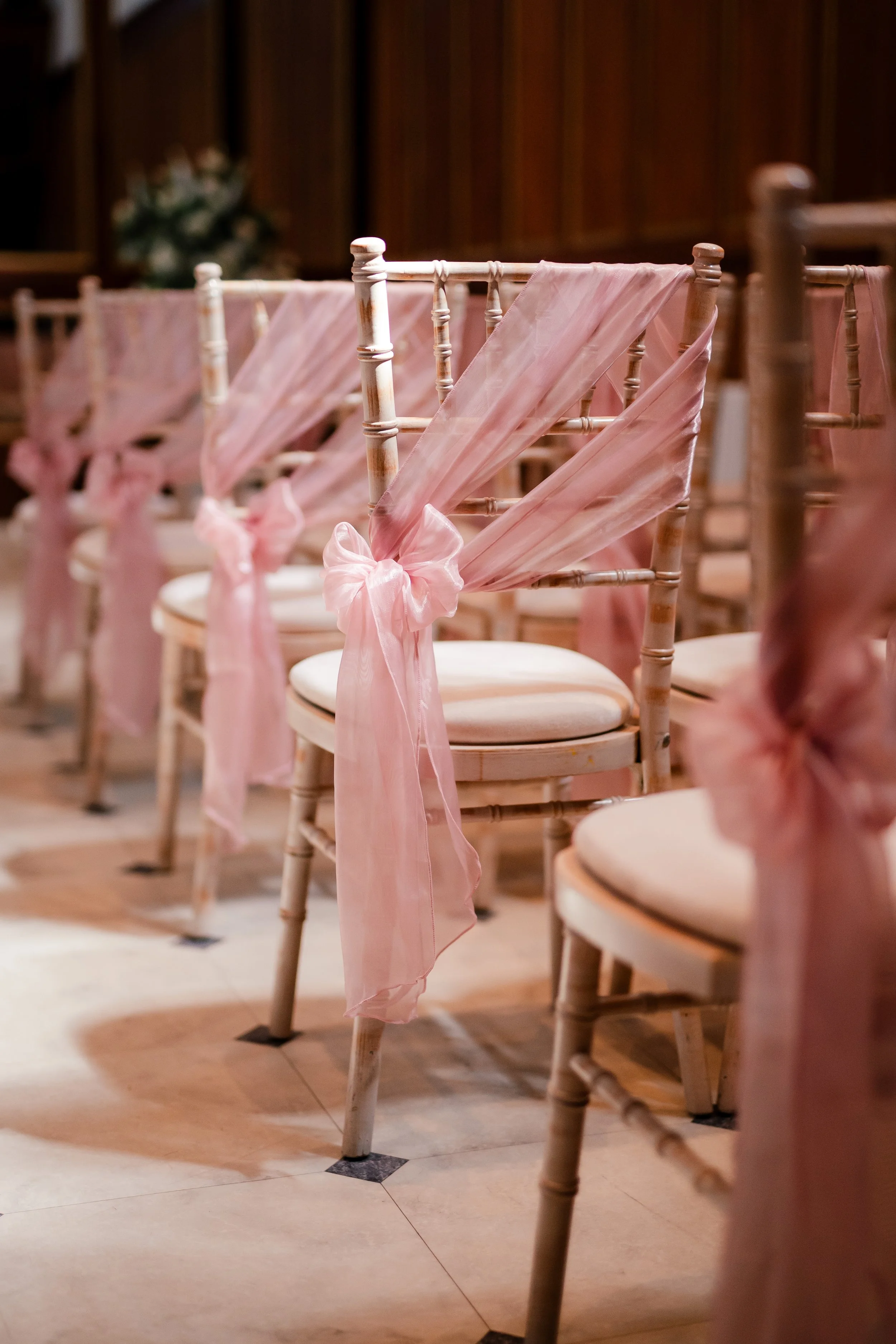 Rows of chairs decorated with pink fabric sashes tied in bows, set up for a wedding or event.