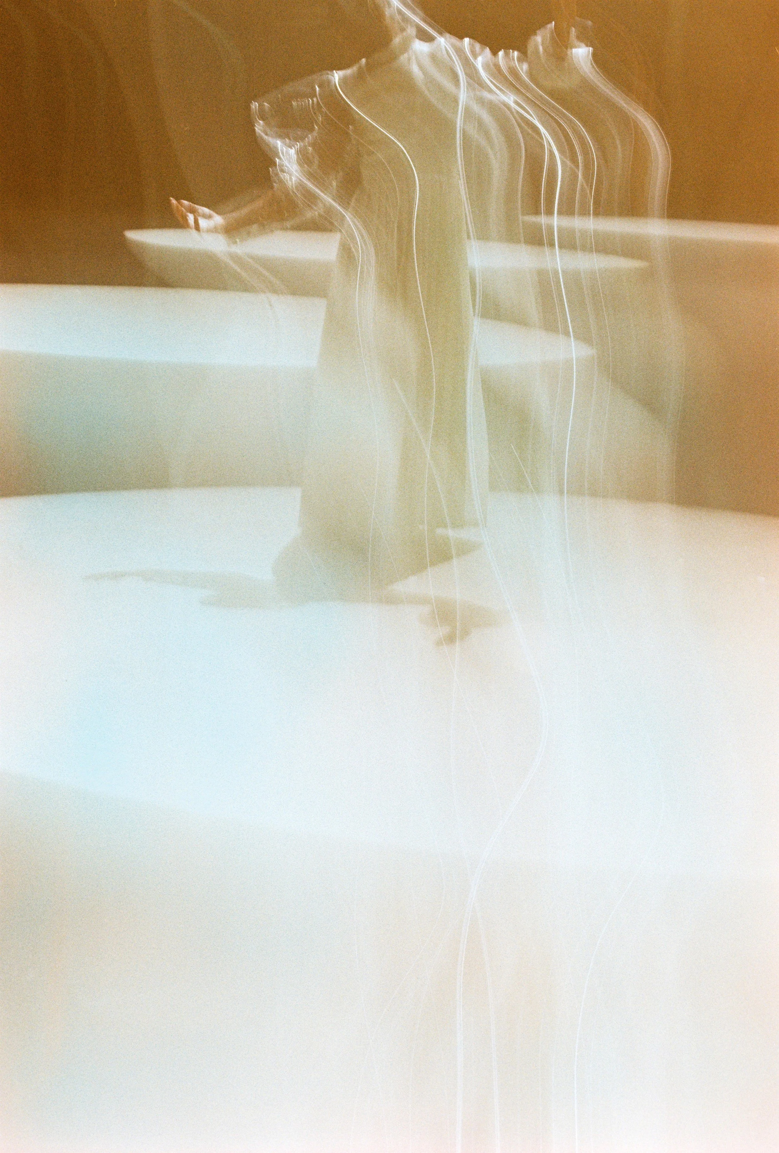 A woman in a gray dress is standing at a table, with a blurred, light streaked effect in the photo.