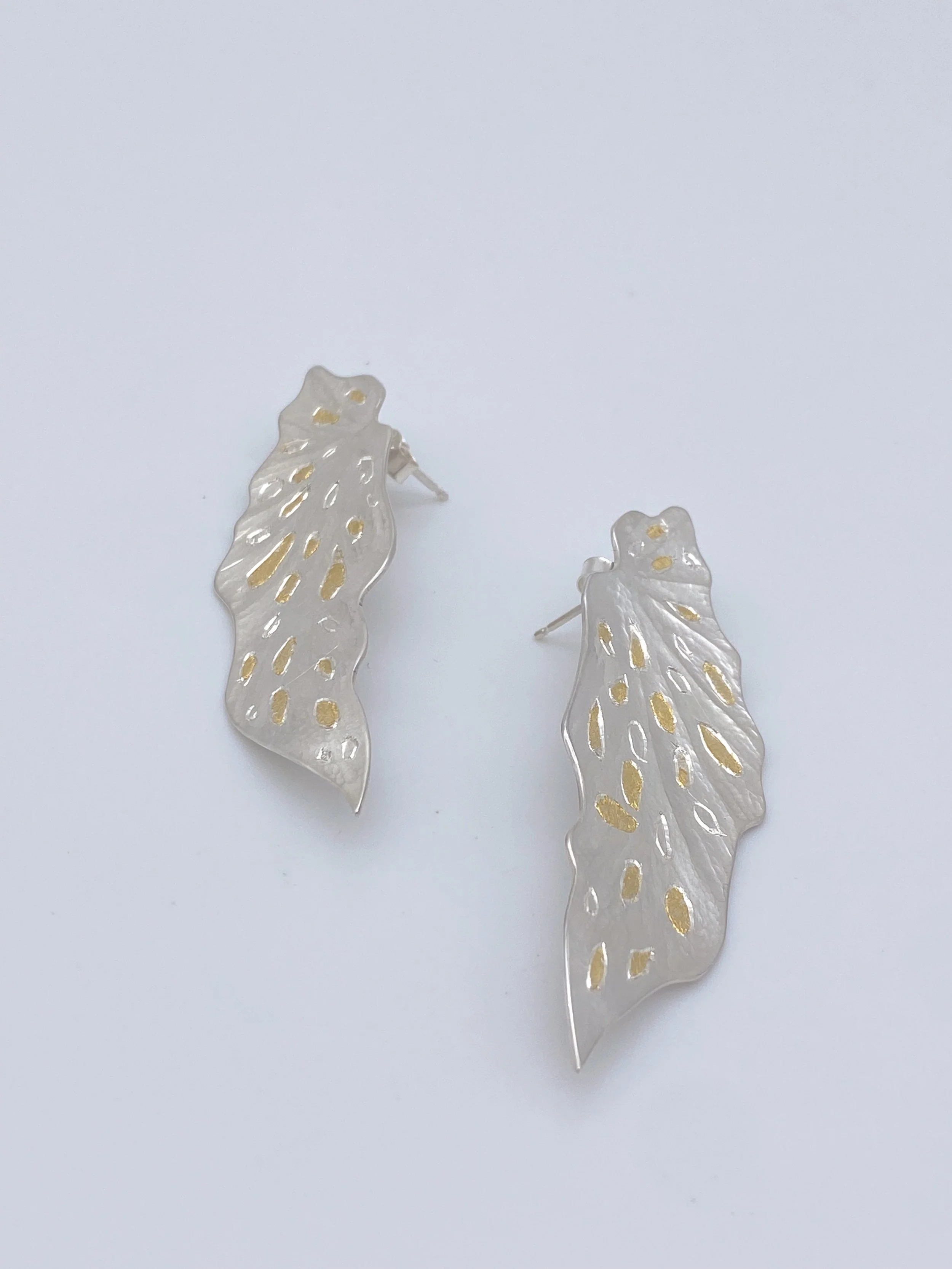 Silver leaf-shaped earrings with gold accents on a plain white background.