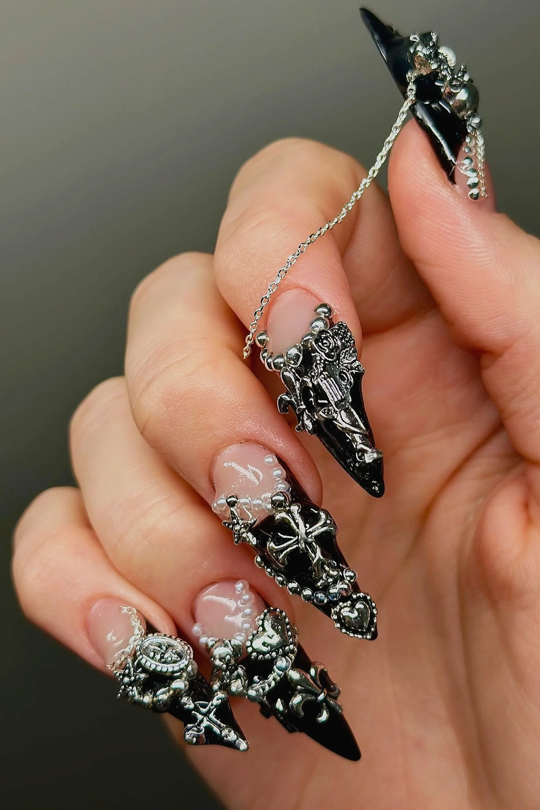 Close-up of a hand with decorated nails holding a silver chain with four black dagger-shaped pendants featuring intricate designs and symbols.