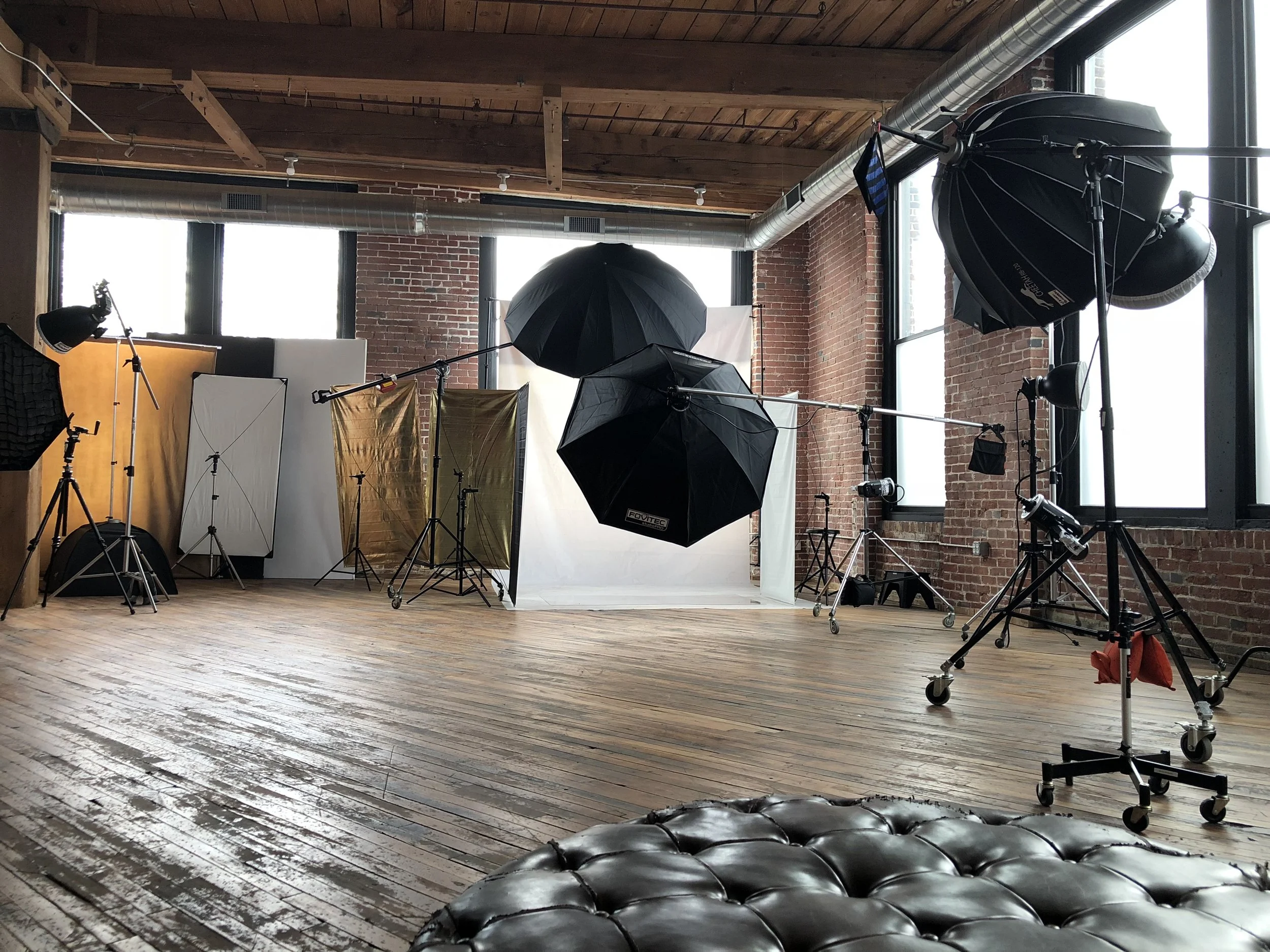 Photography studio with professional lighting equipment, umbrellas, and a backdrop in a loft-style space with brick walls and wooden floors.