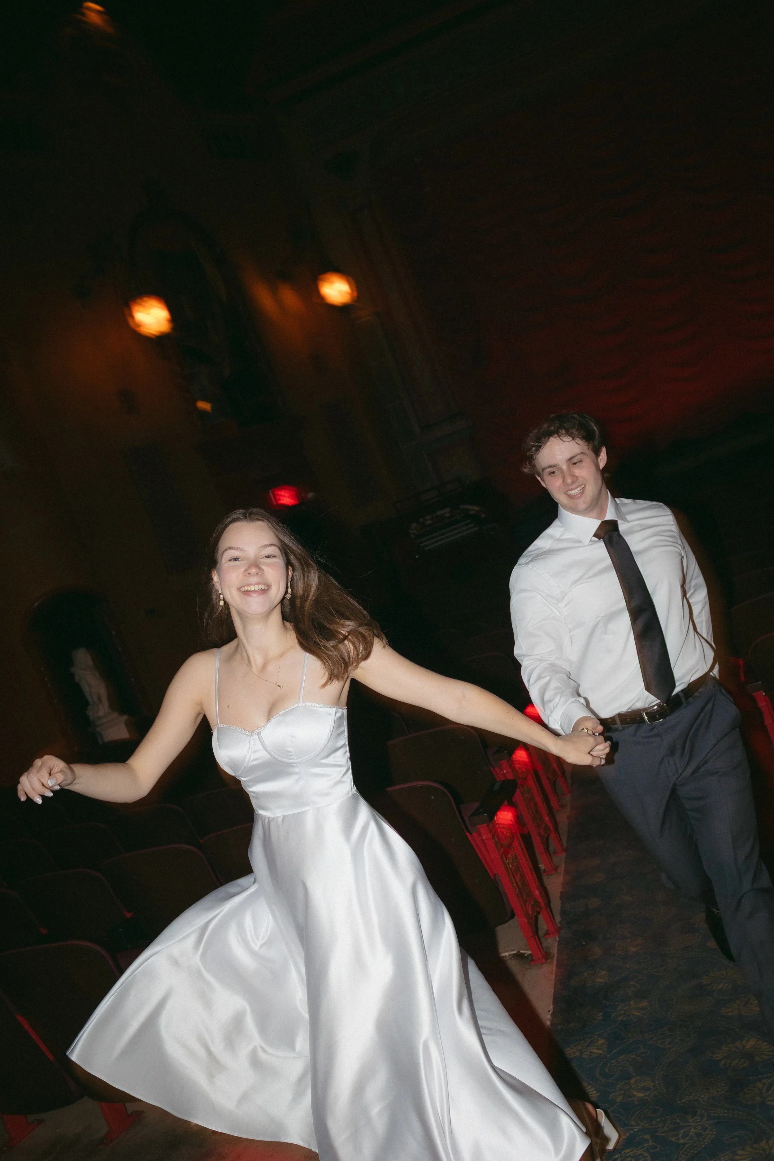 couple running in white dress & tux in old theathre