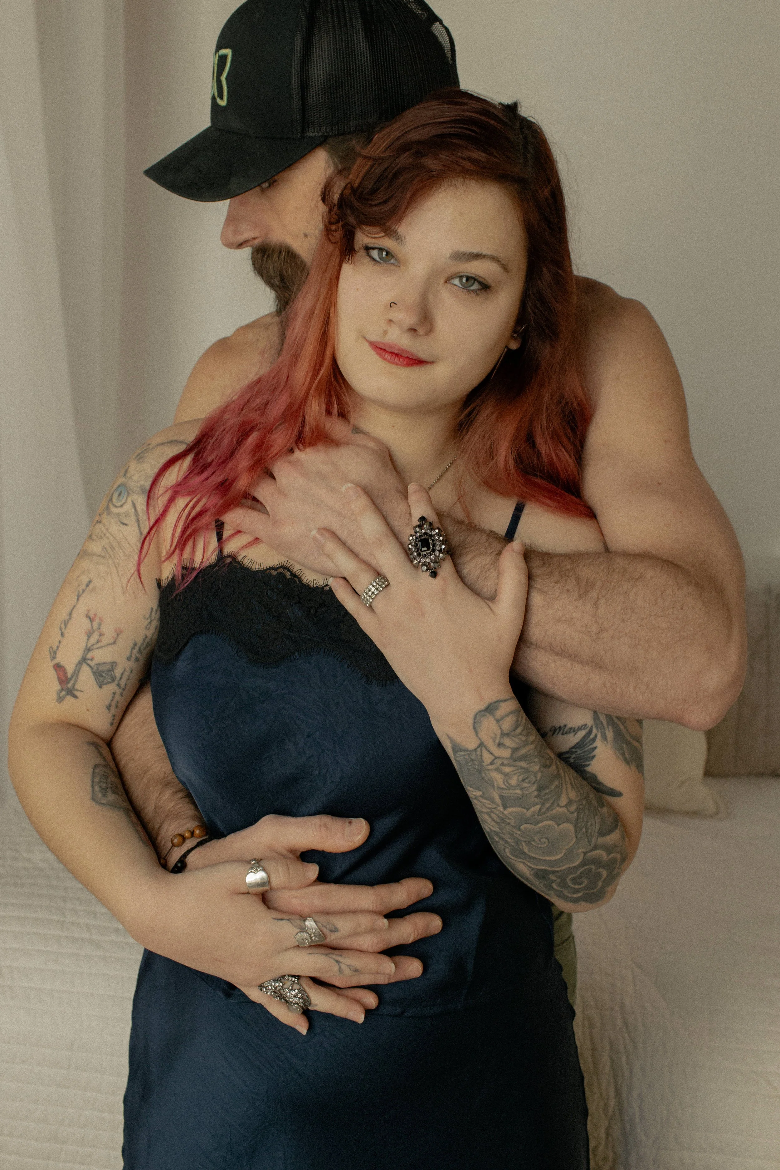 man in a baseball cap posing in a couples boudoir photography session with girl in dark blue dress