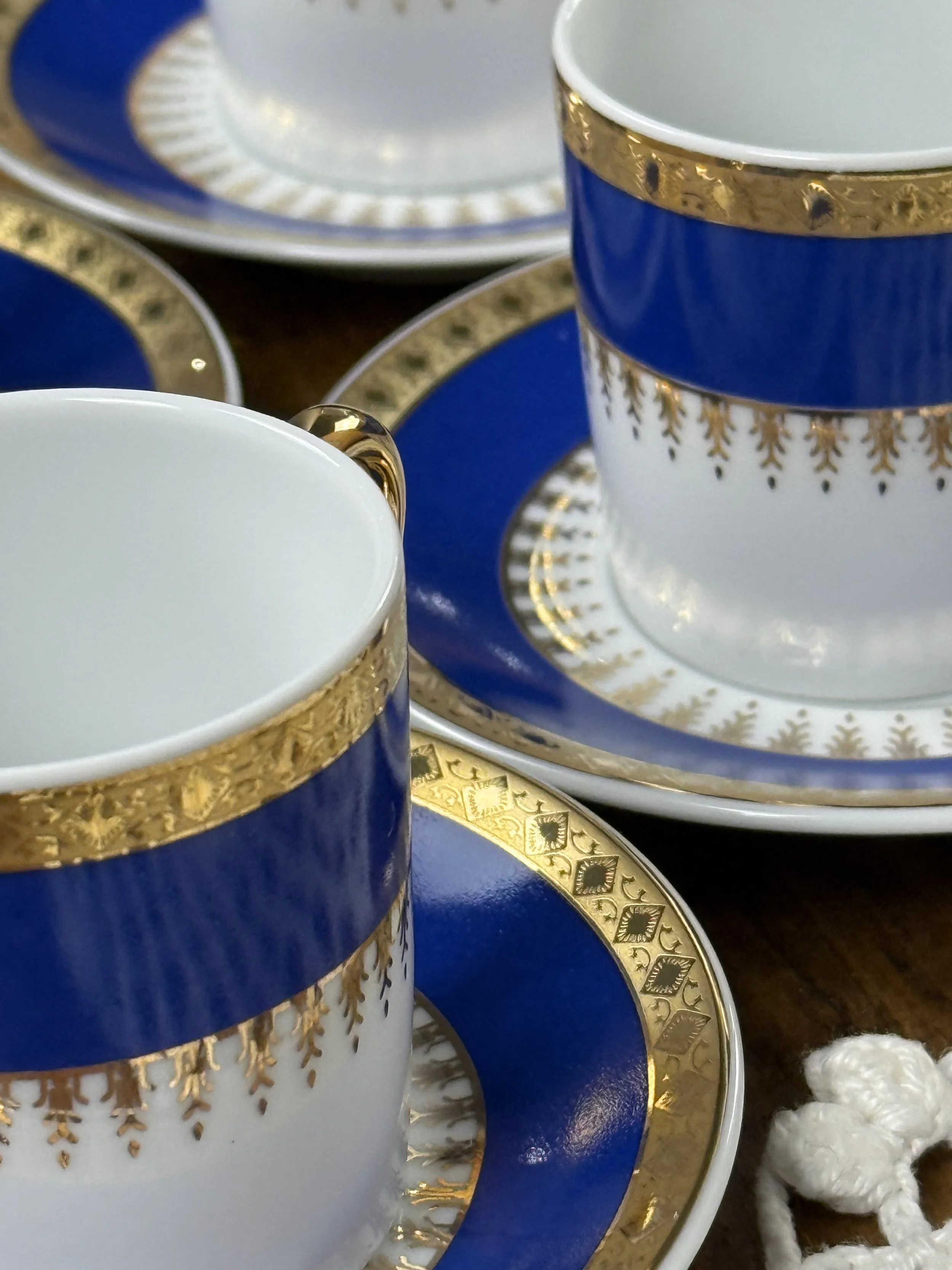 Close-up of vintage espresso cup showing cobalt blue band, intricate gold detailing, and luminous gilt handle on white porcelain