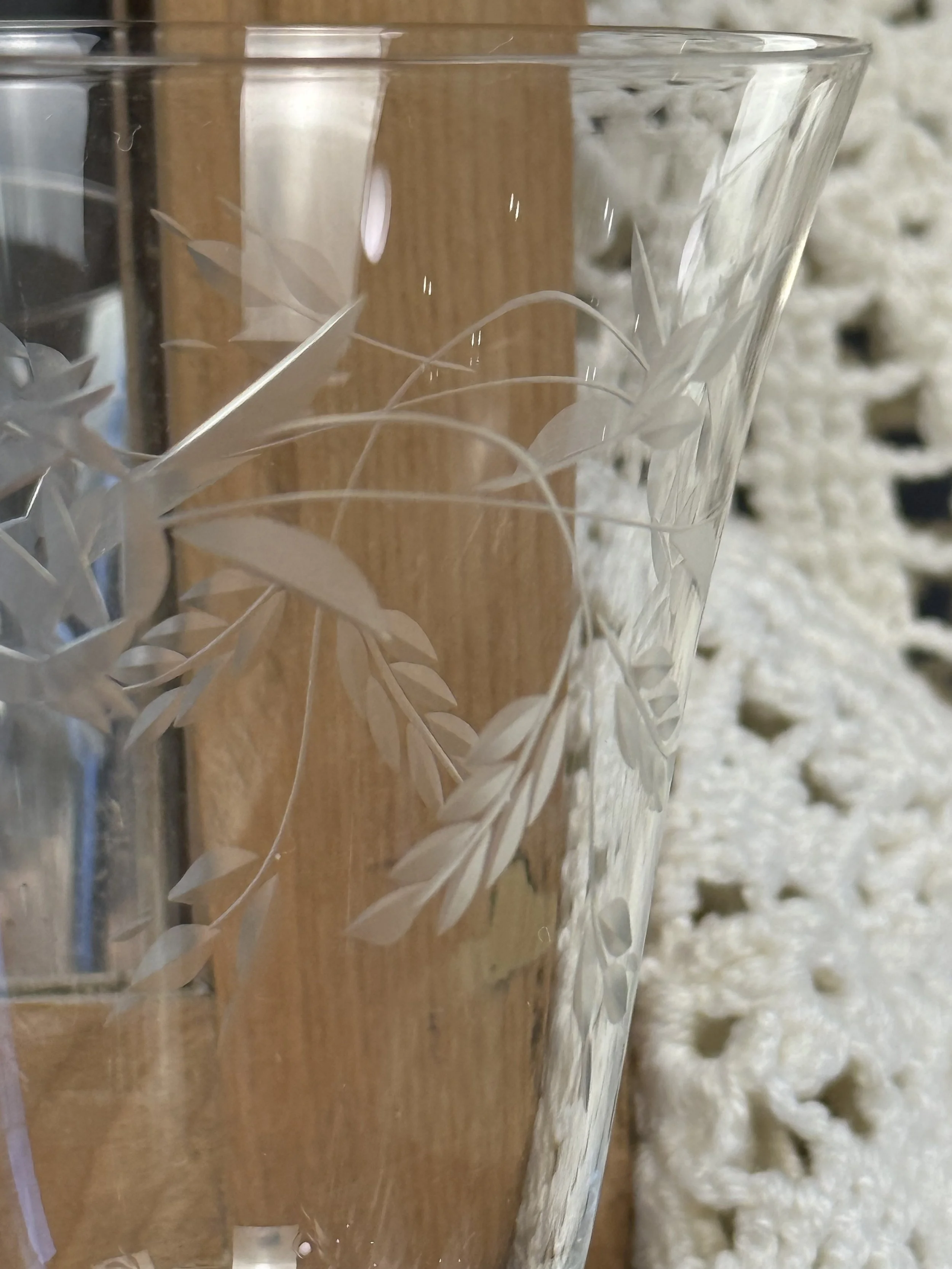 Close-up of vintage etched cocktail glass with botanical leaf pattern, clear stemmed glass showing hand-etched floral design and smooth rim
