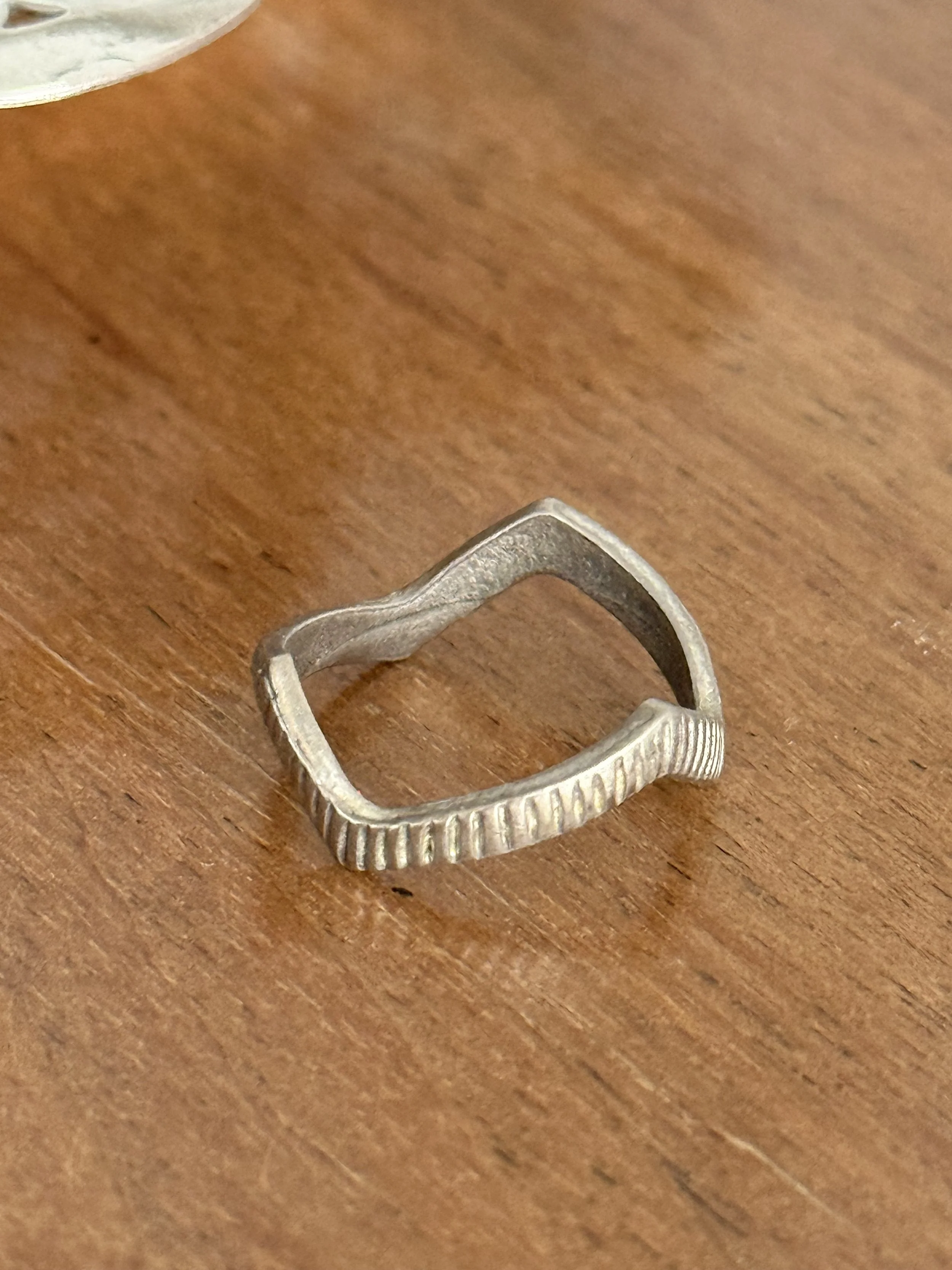 Close-up of vintage silver geometric ring on wooden surface, ridged textured band and open sculptural form