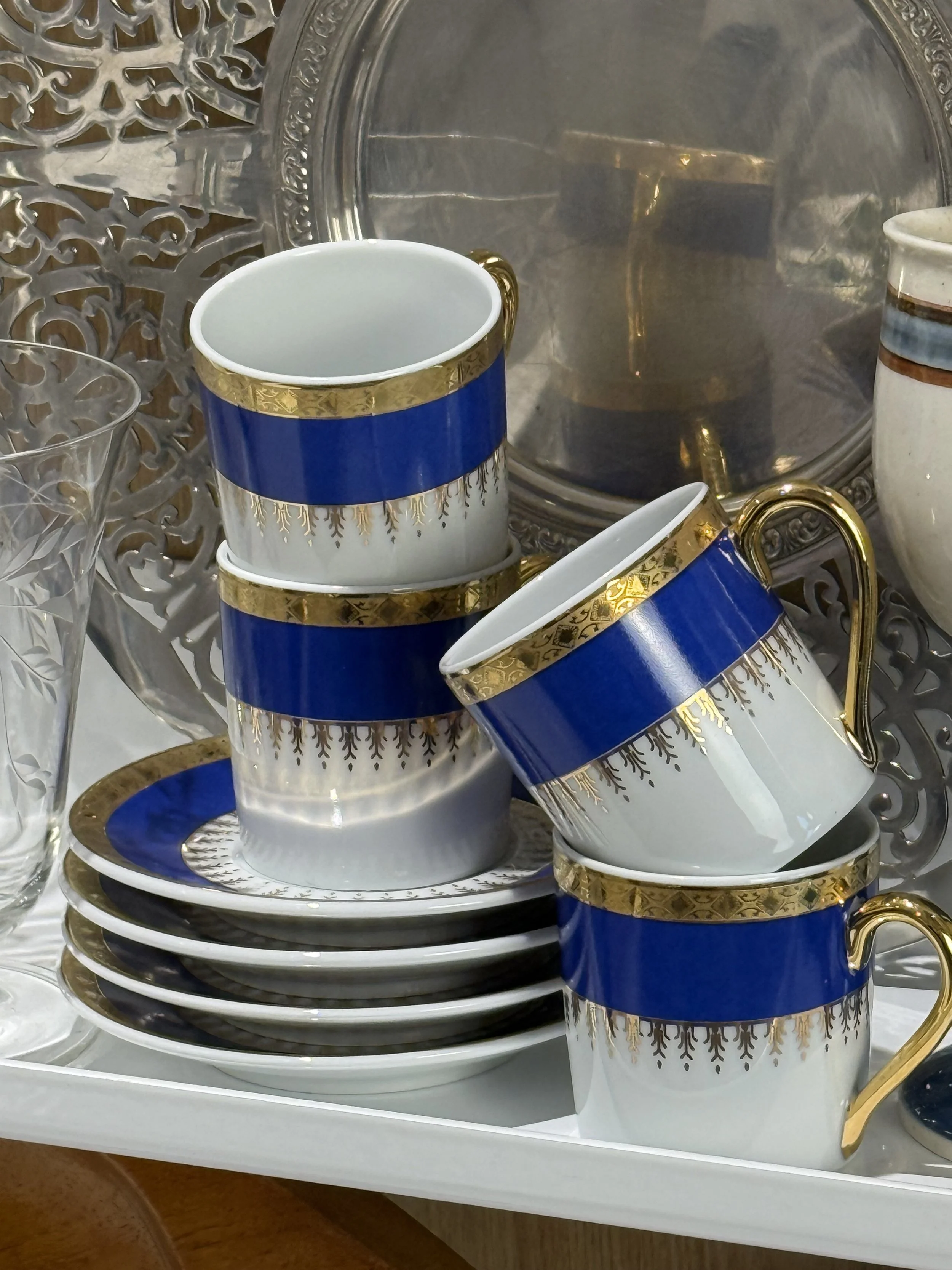 Styled arrangement of vintage blue and gold porcelain espresso cups and saucers on shelving, elegant old-world coffee presentation