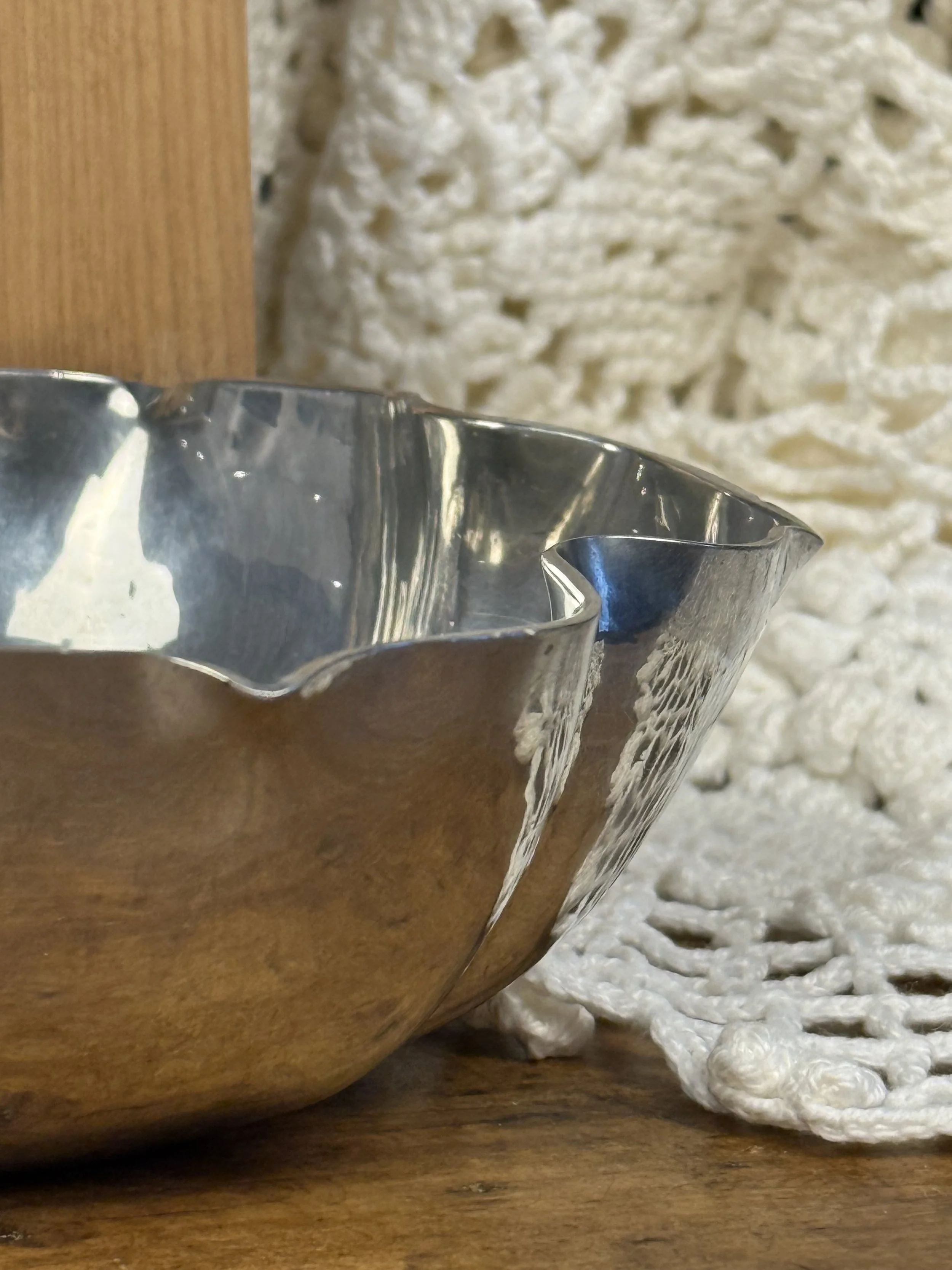 Close-up of scalloped rim detail on vintage silver bowl, hand-formed edge with fluid curves and polished reflective finish