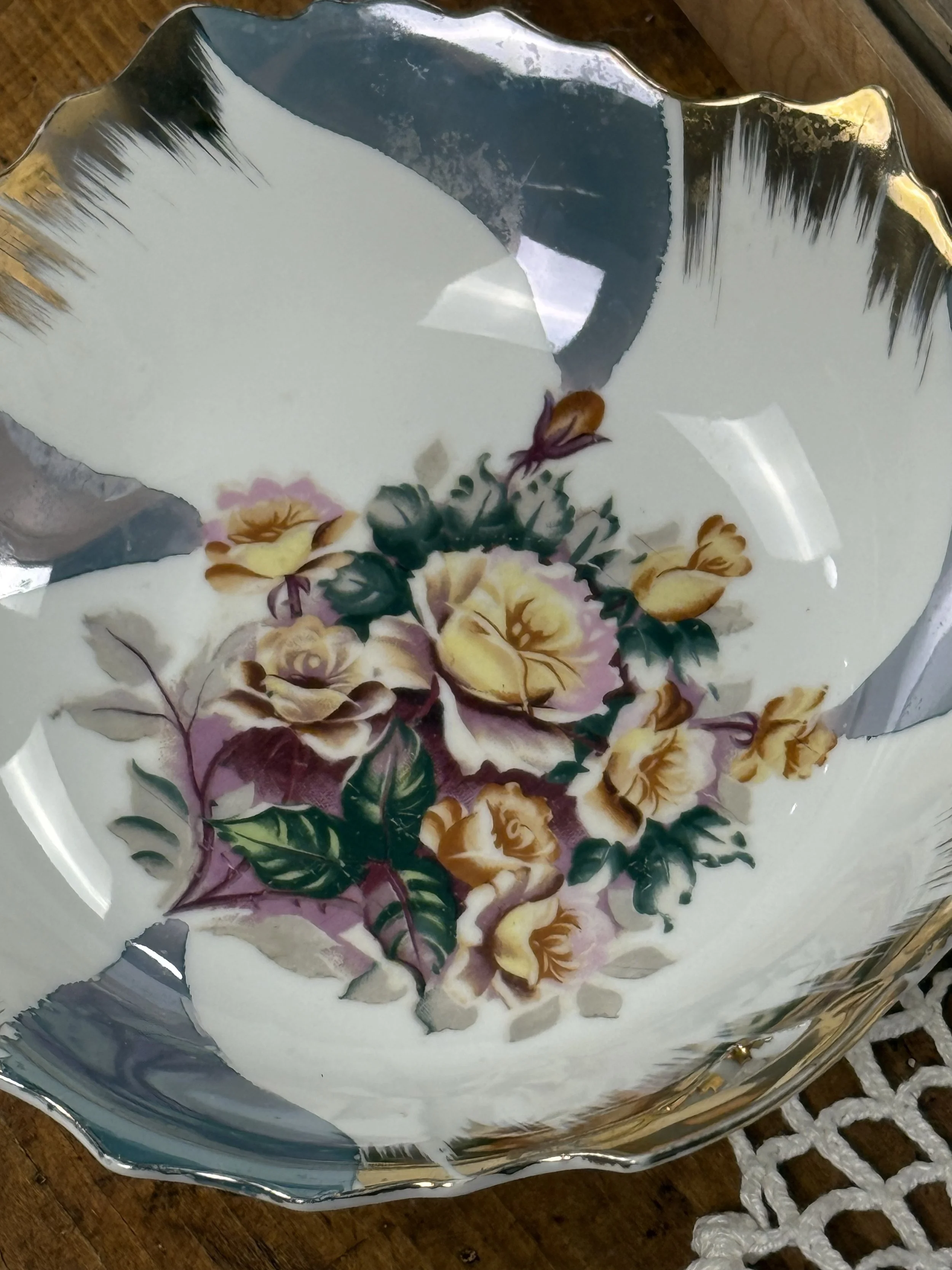 Top-down view of vintage floral porcelain plate with hand-painted rose bouquet centerpiece, soft blush, cream, and green tones, framed by abstract grey-blue glaze and gold scalloped edge