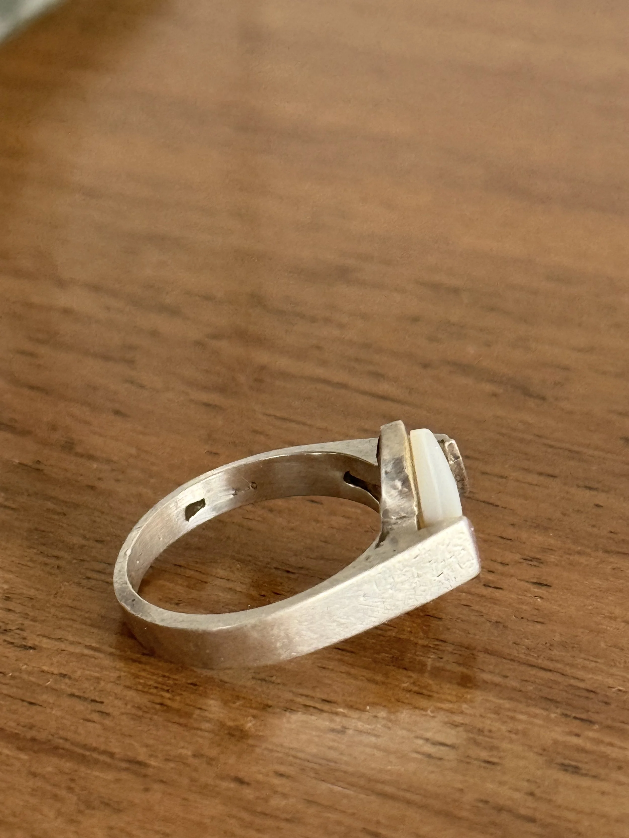 Profile view of handcrafted silver ring with raised marquise white stone setting and split shoulders, vintage modernist jewelry on wooden surface