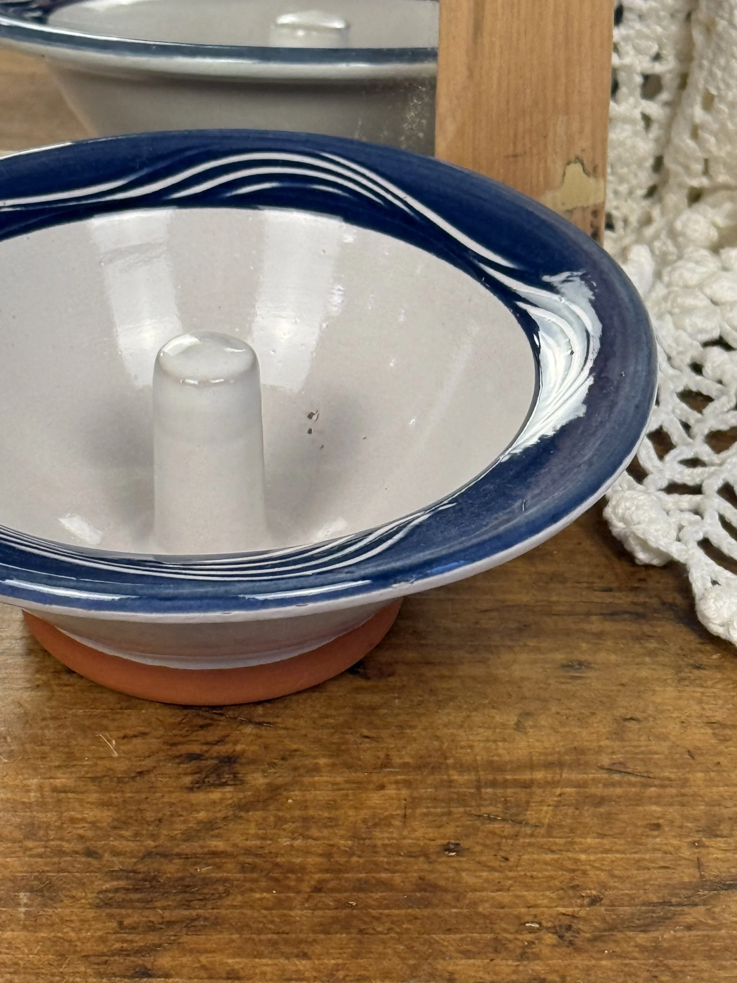 Top view of vintage apple baker dish with raised center chimney, glazed interior, navy blue rim with hand-painted stripe accents, rustic country kitchen bakeware