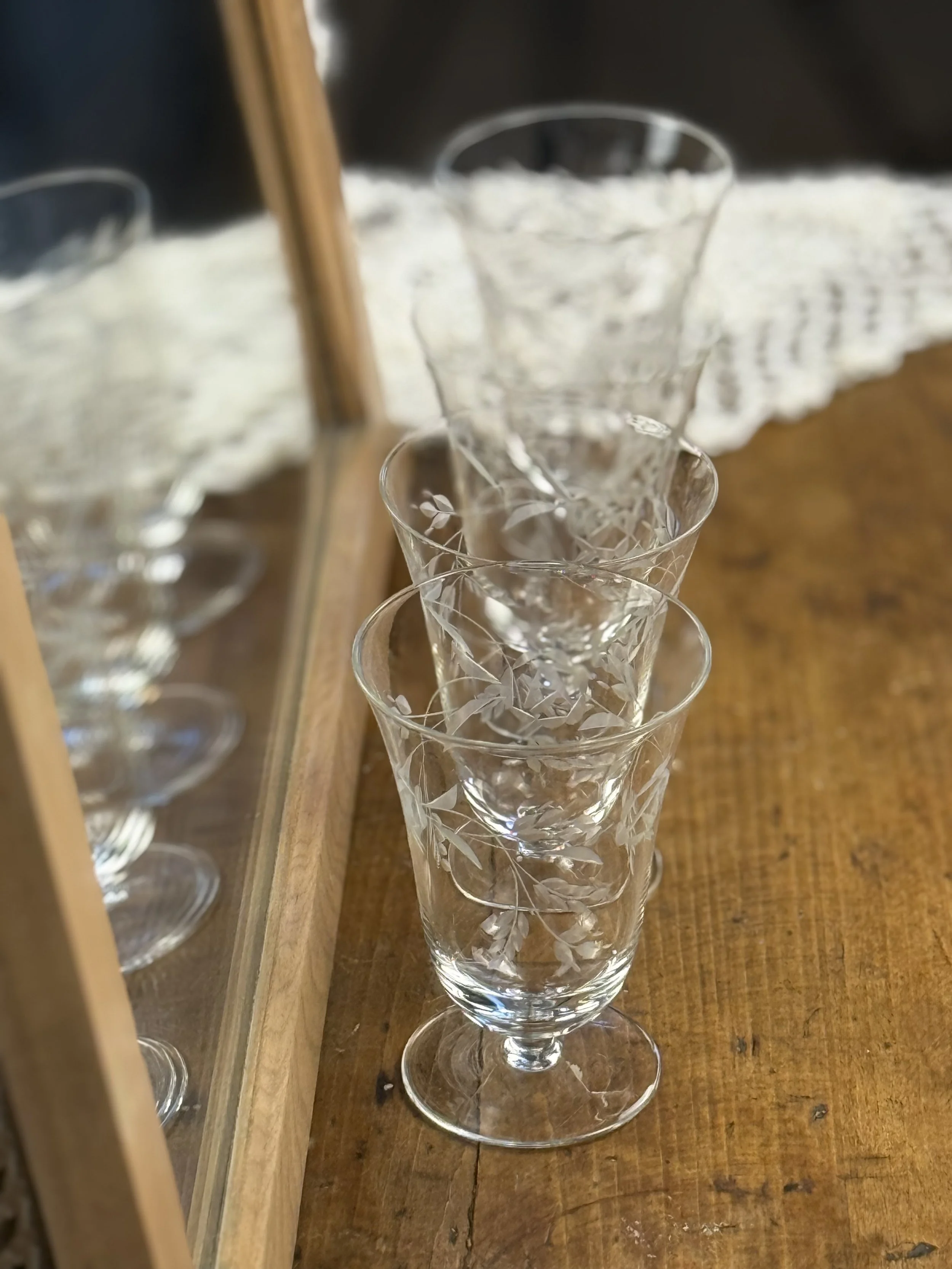 Stacked view of vintage etched floral cocktail glasses, transparent glass with fine leaf motif engraving, refined mid-century drinkware detail