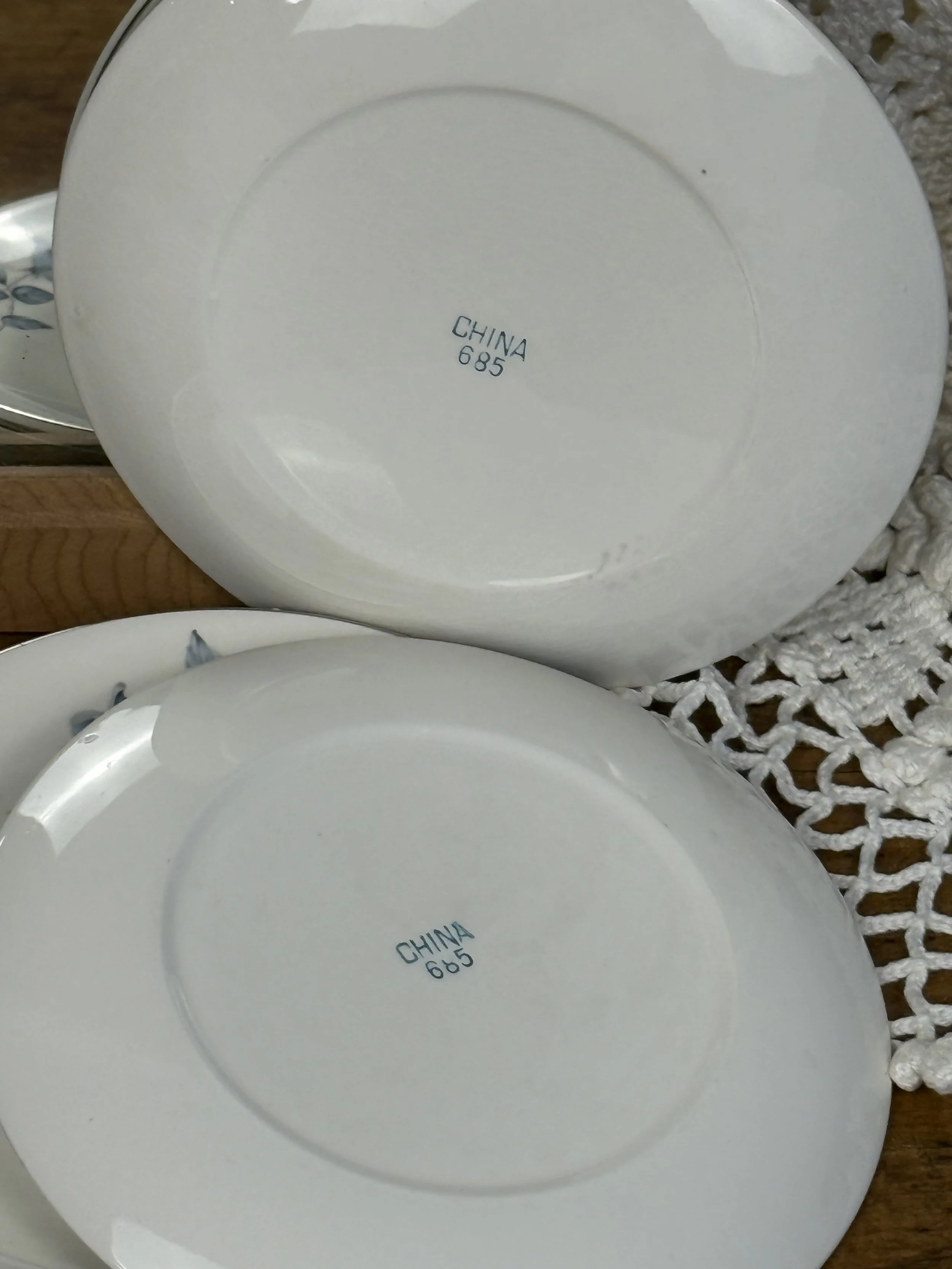 Angled close-up of dessert plate rim and surface, showcasing blue rose floral accents, silver-toned edge, and subtle crazing consistent with late 20th century porcelain