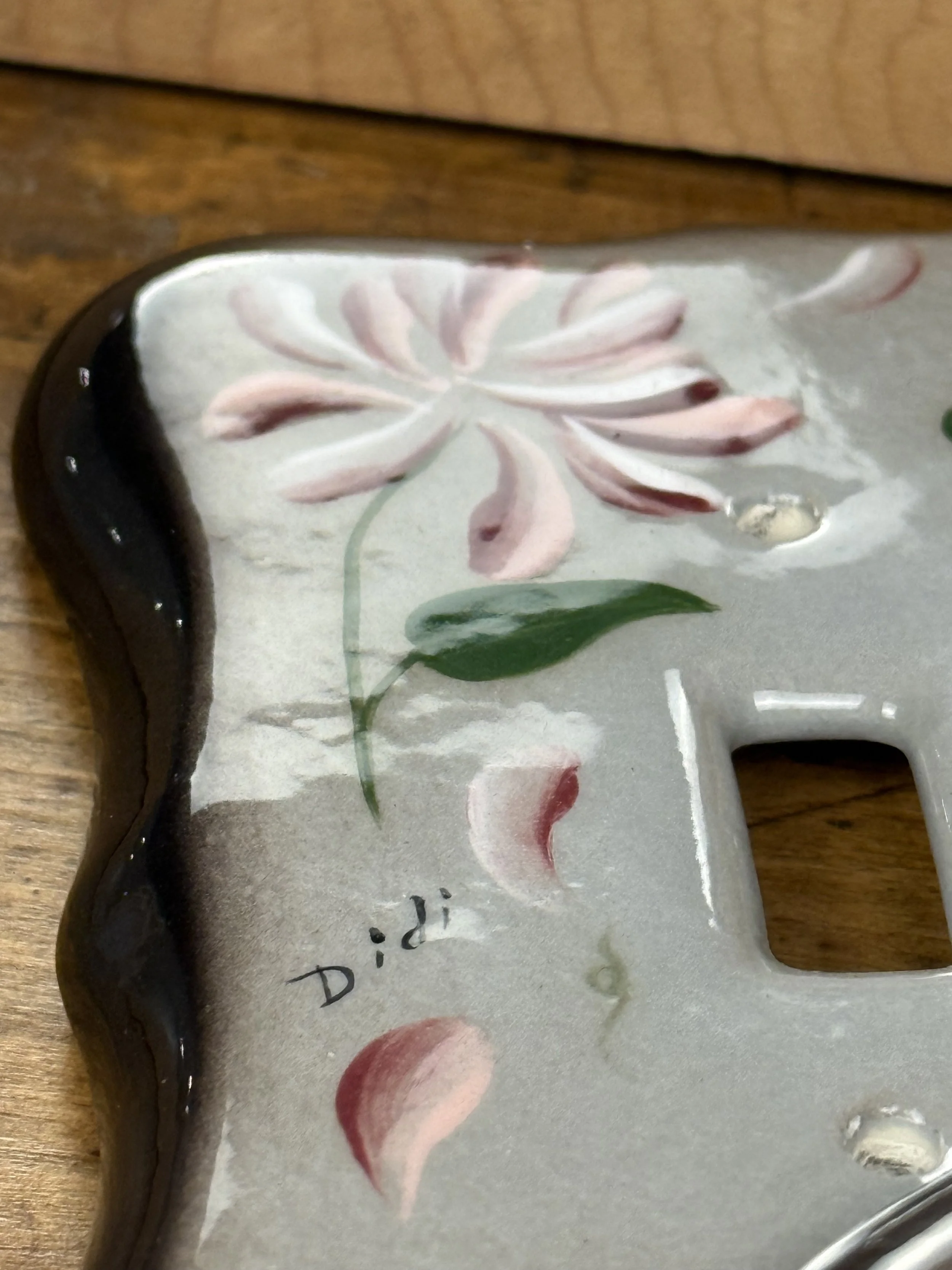 Close-up of hand-painted pink flower and green leaf detail on ceramic light switch plate, glossy glaze, artisan floral design