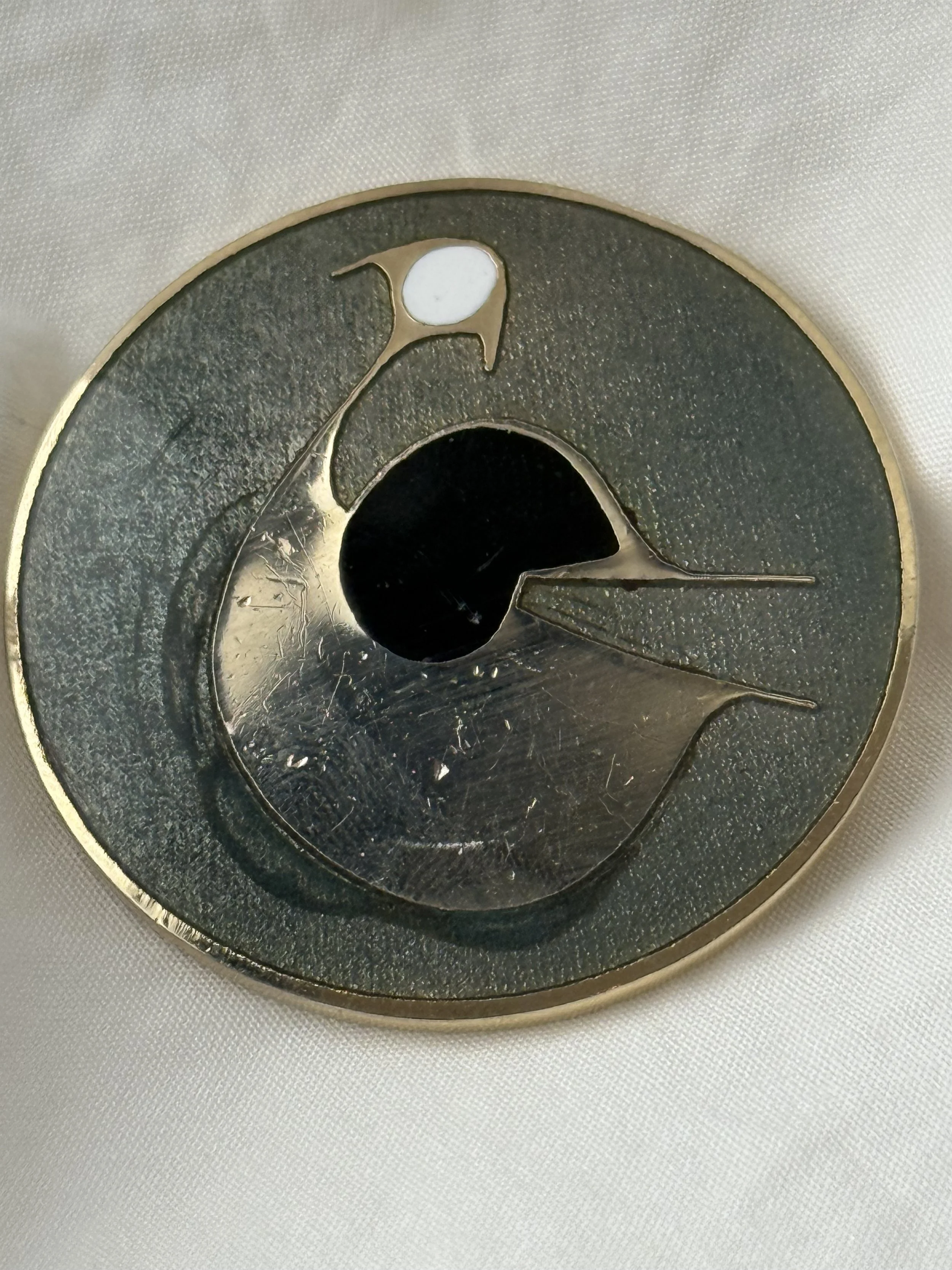 Detailed view of brass bird brooch with dark green enamel field, minimalist modernist design, vintage artisan pin