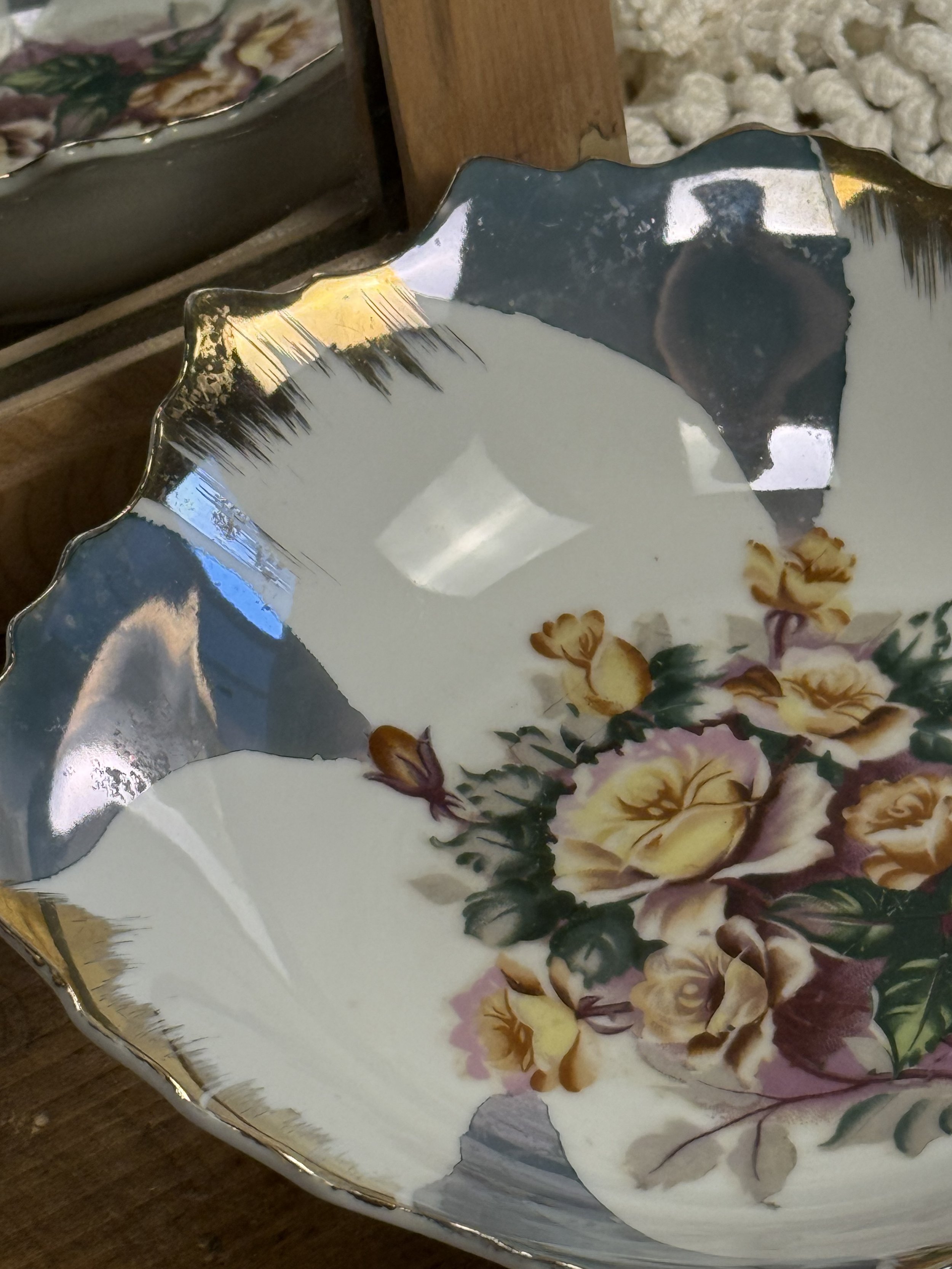 Angled view of vintage porcelain plate highlighting painterly grey-blue glaze fields, gold-edged scalloped rim, and central rose bouquet in muted pastel tones
