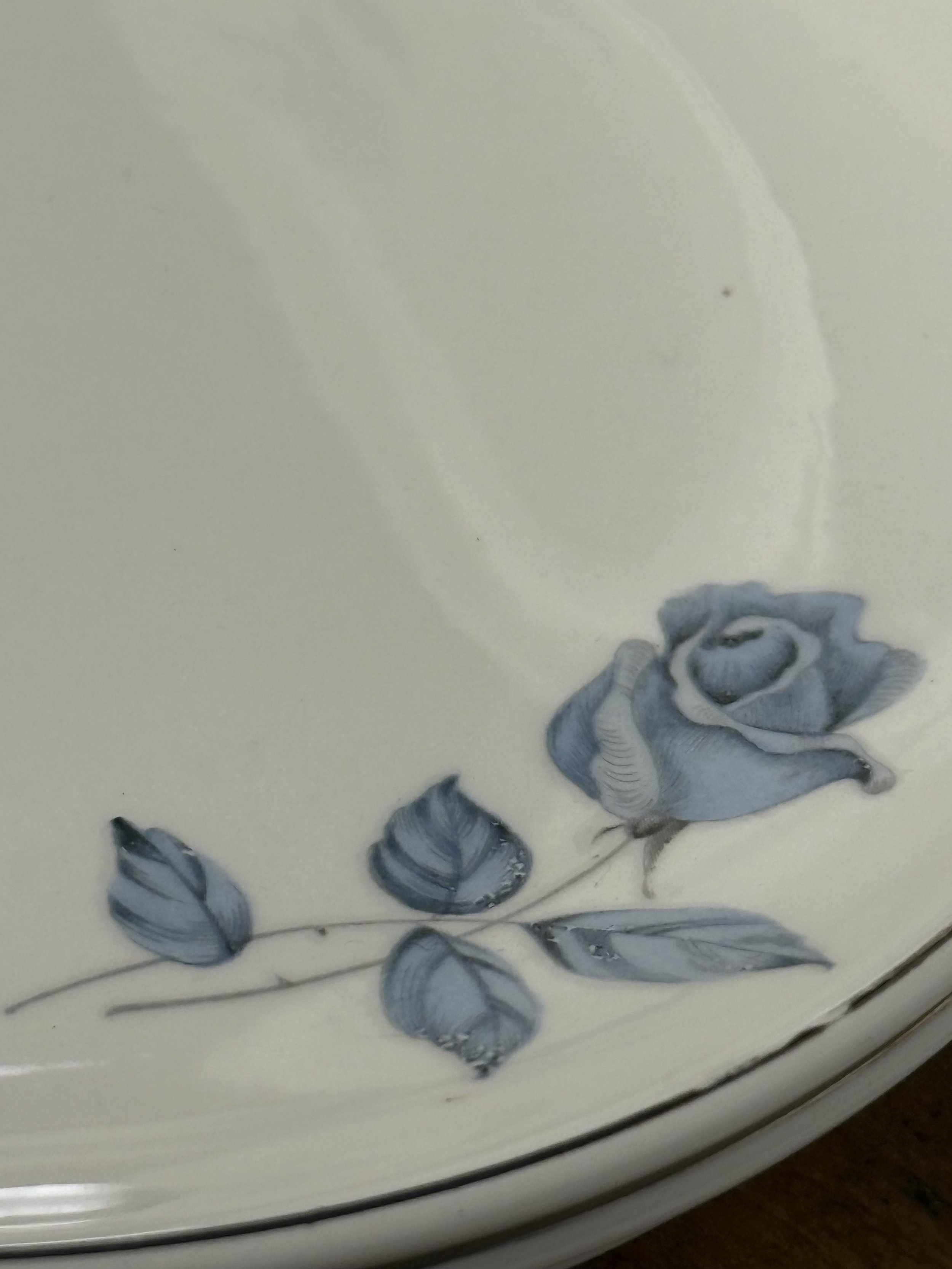 Stacked vintage porcelain dessert plates showing side profile and layered rims, blue rose decoration and silver-tone trim creating a classic romantic table setting look