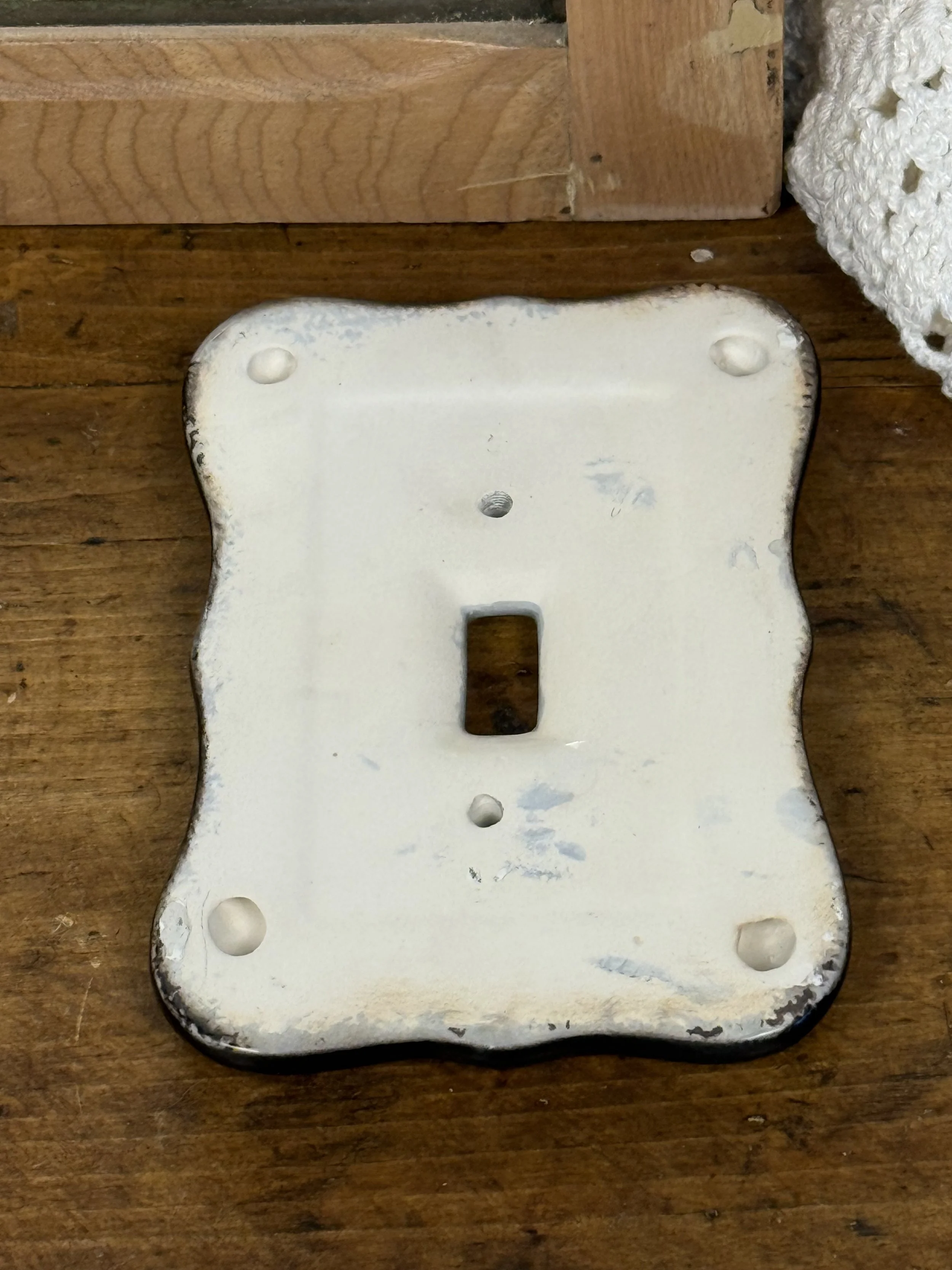 Back view of ceramic light switch plate showing mounting holes, glazed white ceramic underside, vintage hardware component