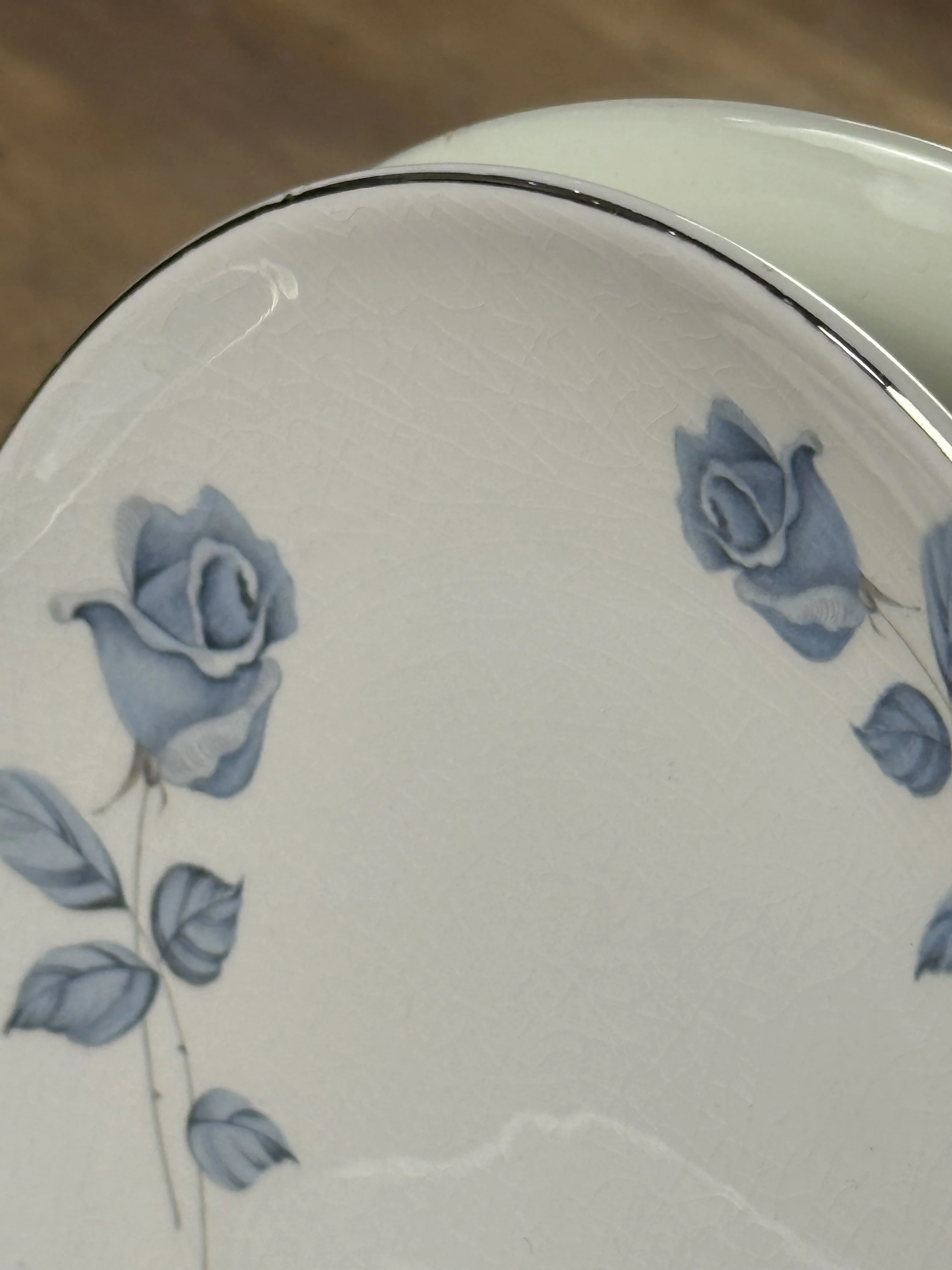 Detail view highlighting light glaze crazing on vintage porcelain dessert plate surface, blue floral rim decoration and silver edging visible, authentic age-related patina