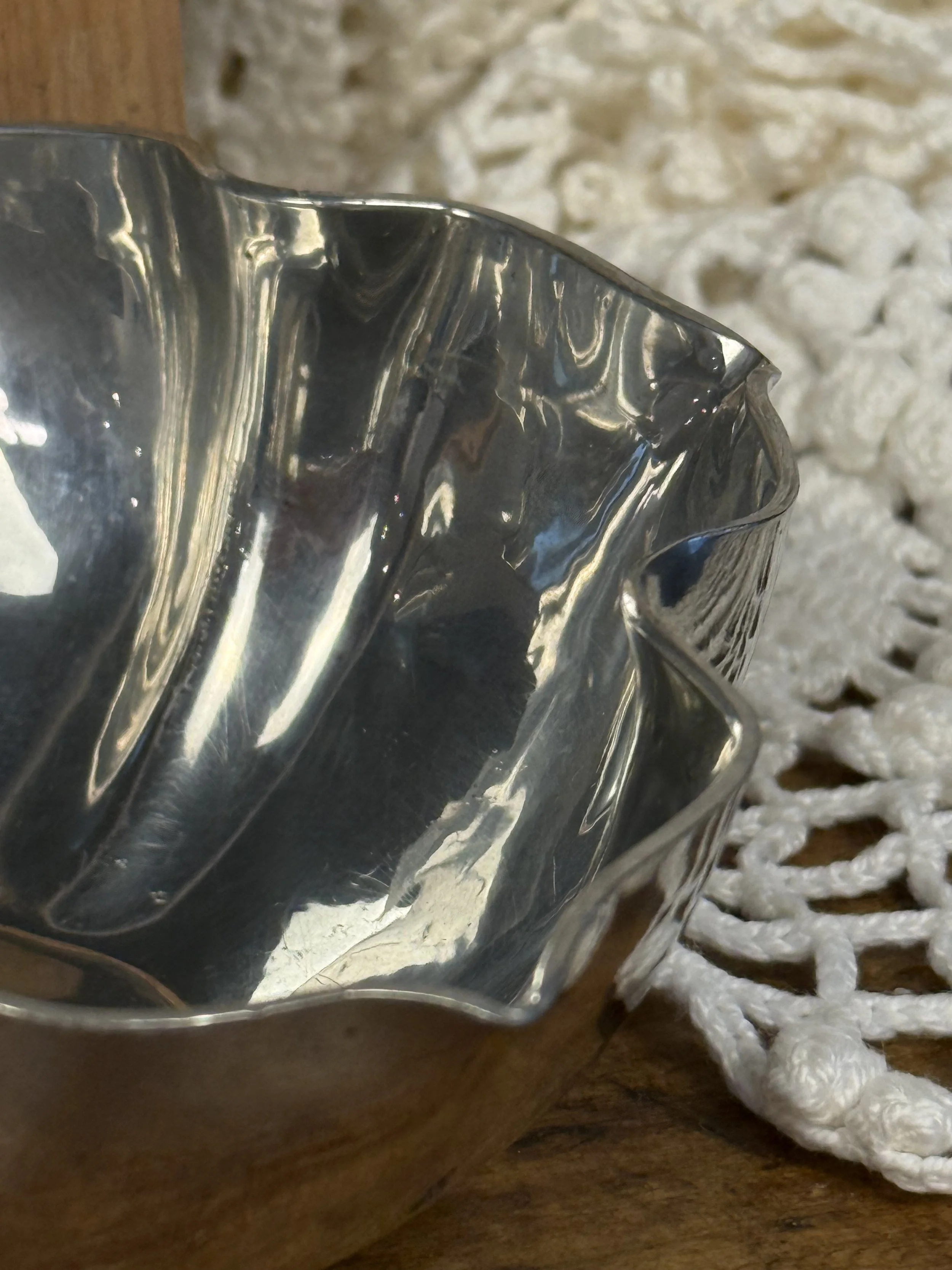 Vintage silver-toned scalloped bowl displayed on wooden surface, organic fluted rim and reflective interior, decorative metal bowl with soft patina