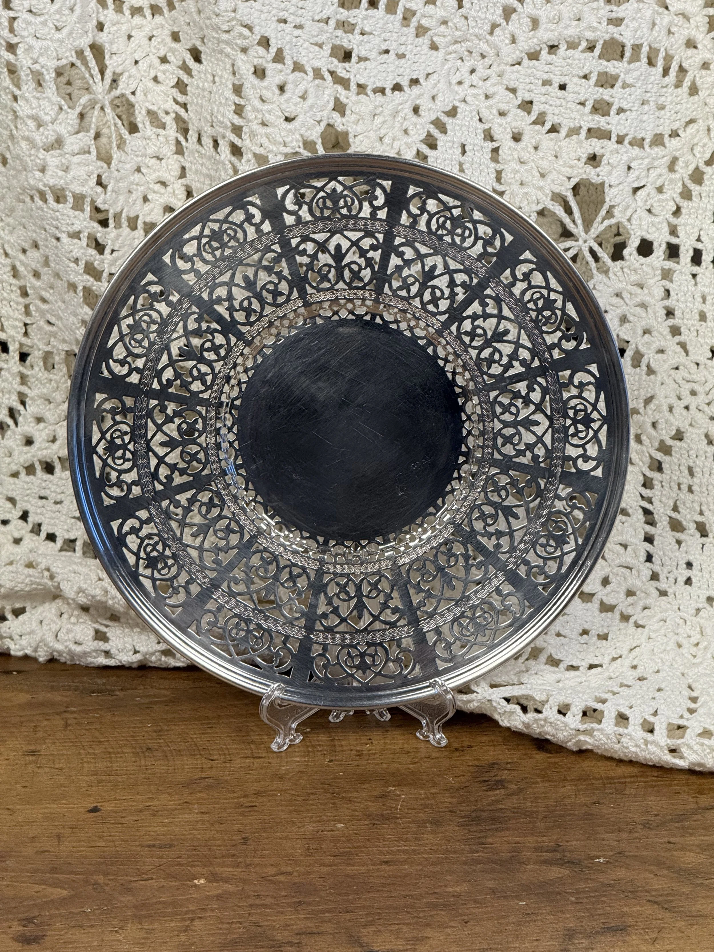 Front view of round vintage silverplate tray on display stand, intricate pierced border and polished center well