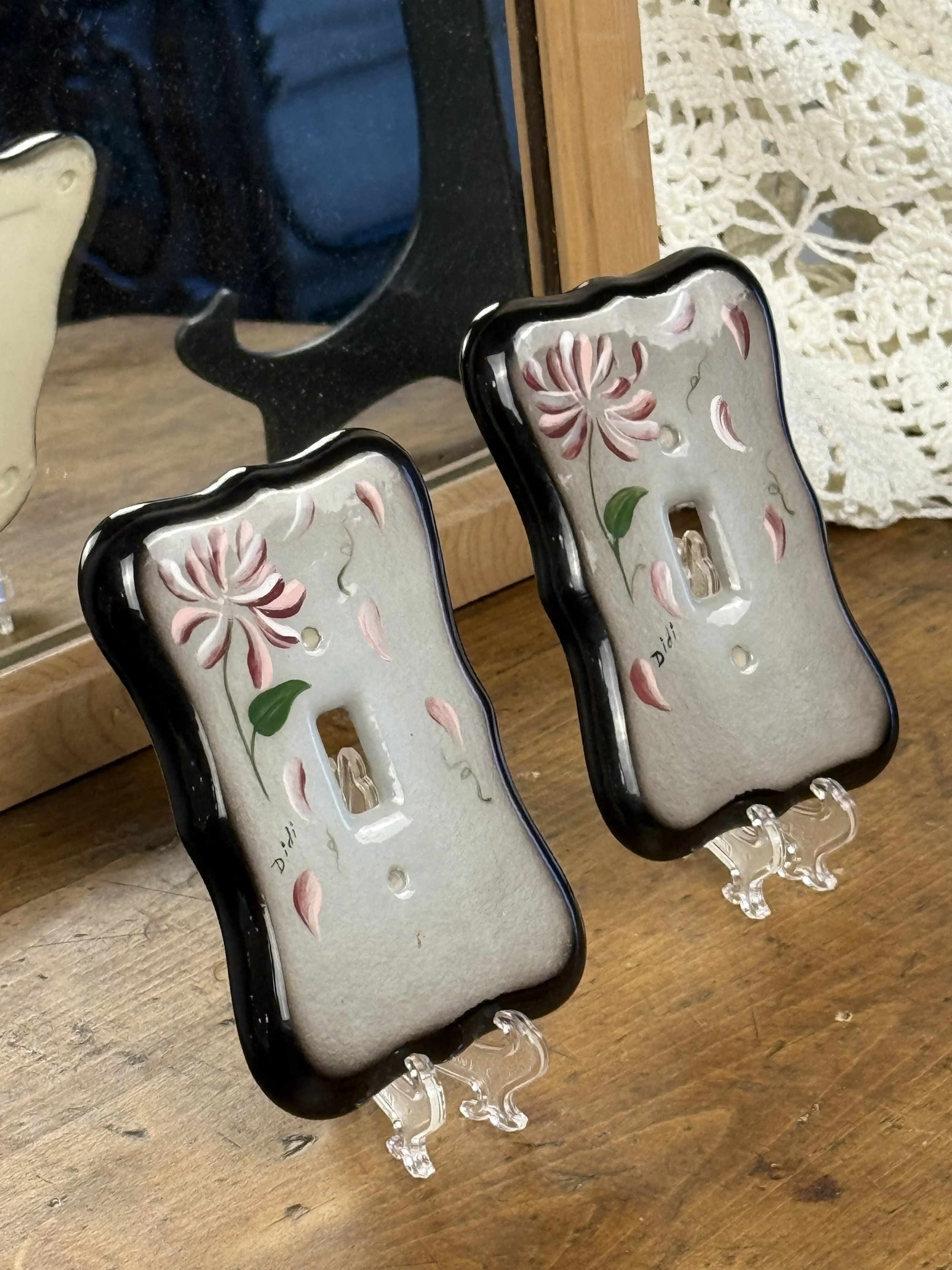 Pair of vintage ceramic light switch covers displayed upright, hand-painted floral pattern, sculpted black border, decorative wall accent