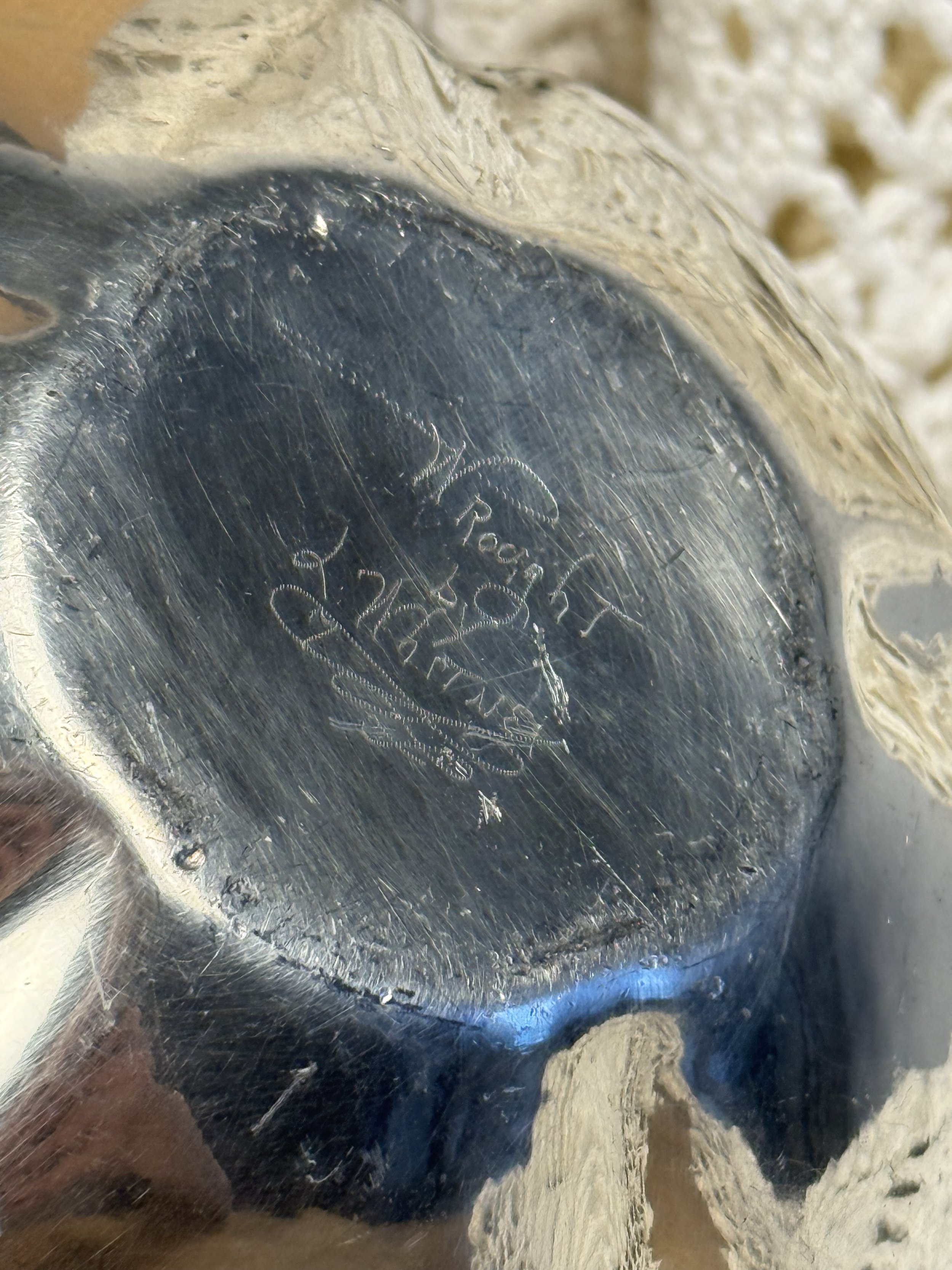 Close-up of engraved hallmark on underside of vintage silver bowl, maker’s mark visible with age-related surface wear