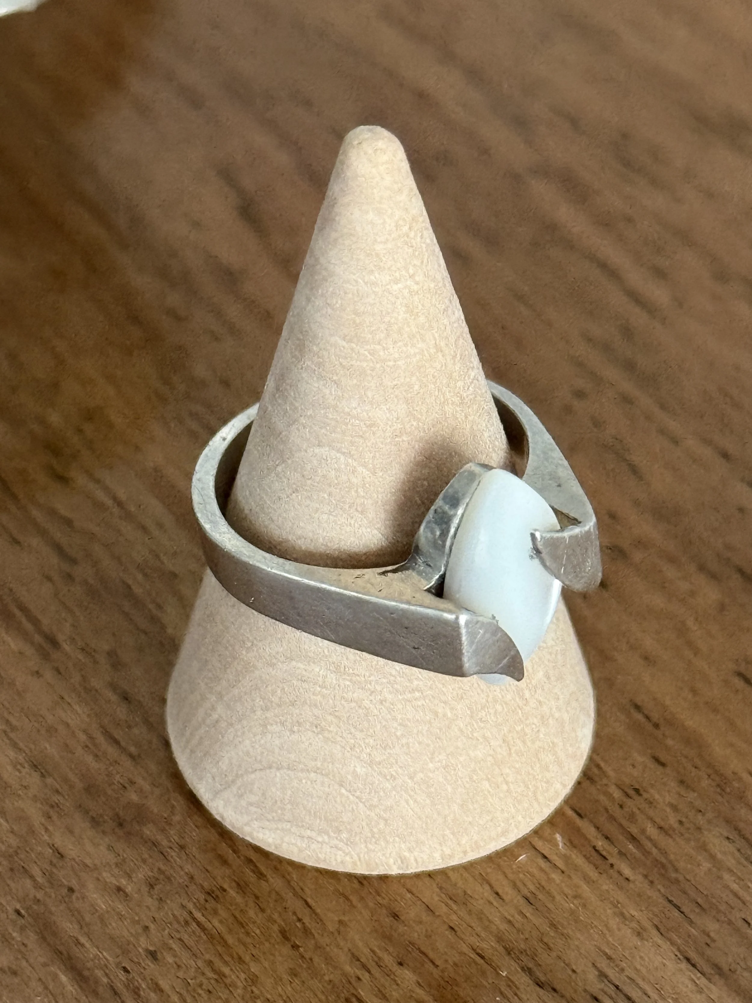 Angled top view of modernist silver ring with marquise white stone and geometric prongs, vintage minimalist jewelry displayed on wooden cone