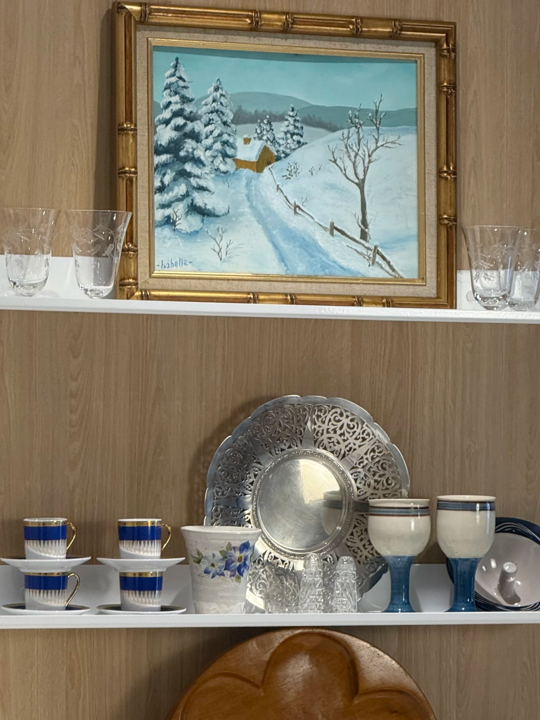 Interior styling view showing framed snowy landscape painting displayed on shelf among vintage tableware