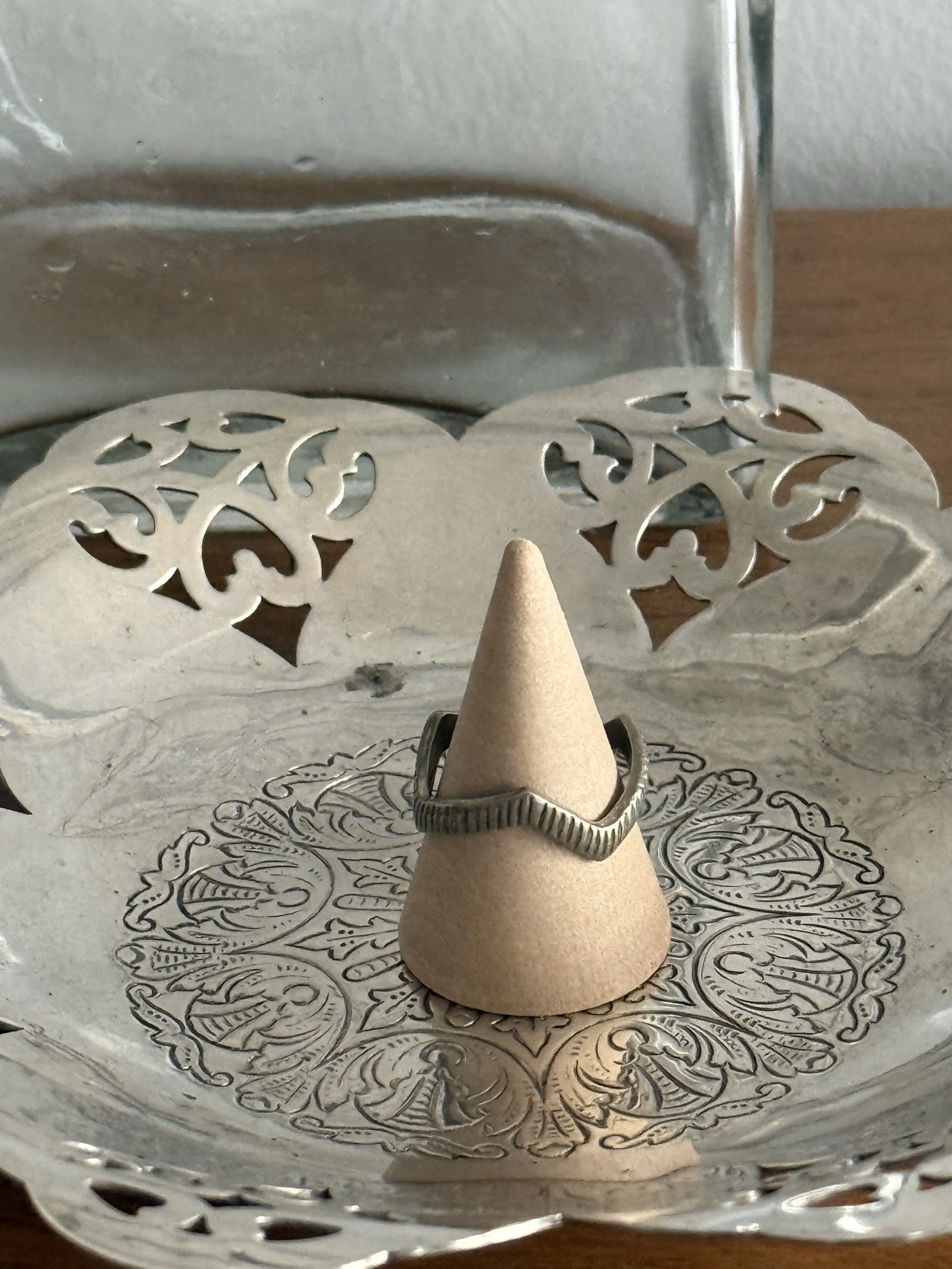 Vintage silver angular band ring resting on decorative metal dish, open geometric construction with ridged texture