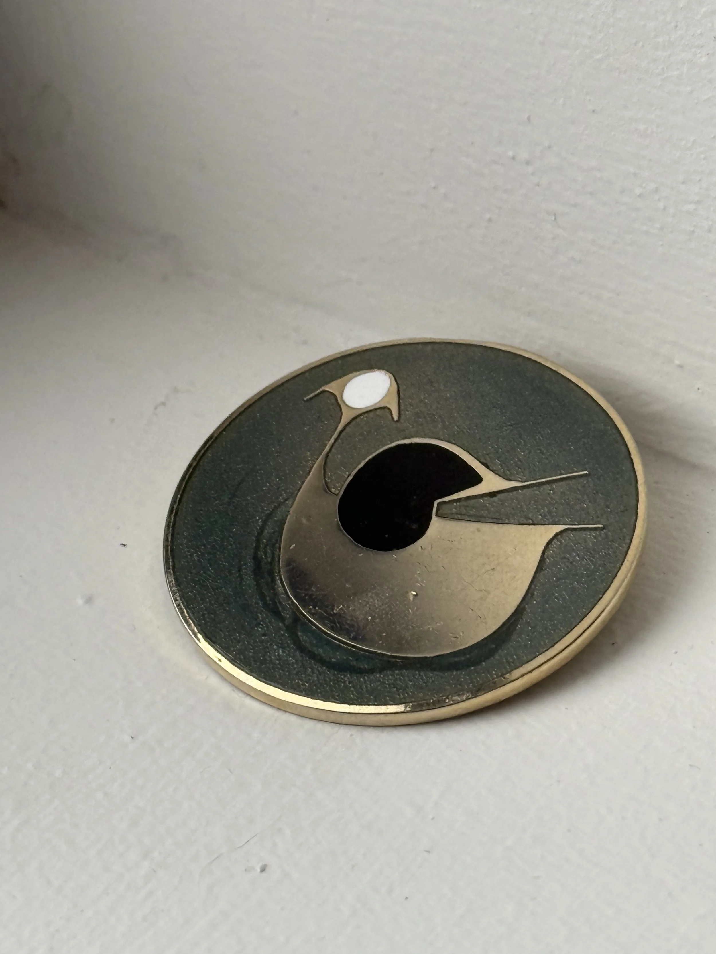 Close-up of vintage enamel bird brooch front, brass cut-out bird with elongated beak, mid-century modern jewelry detail