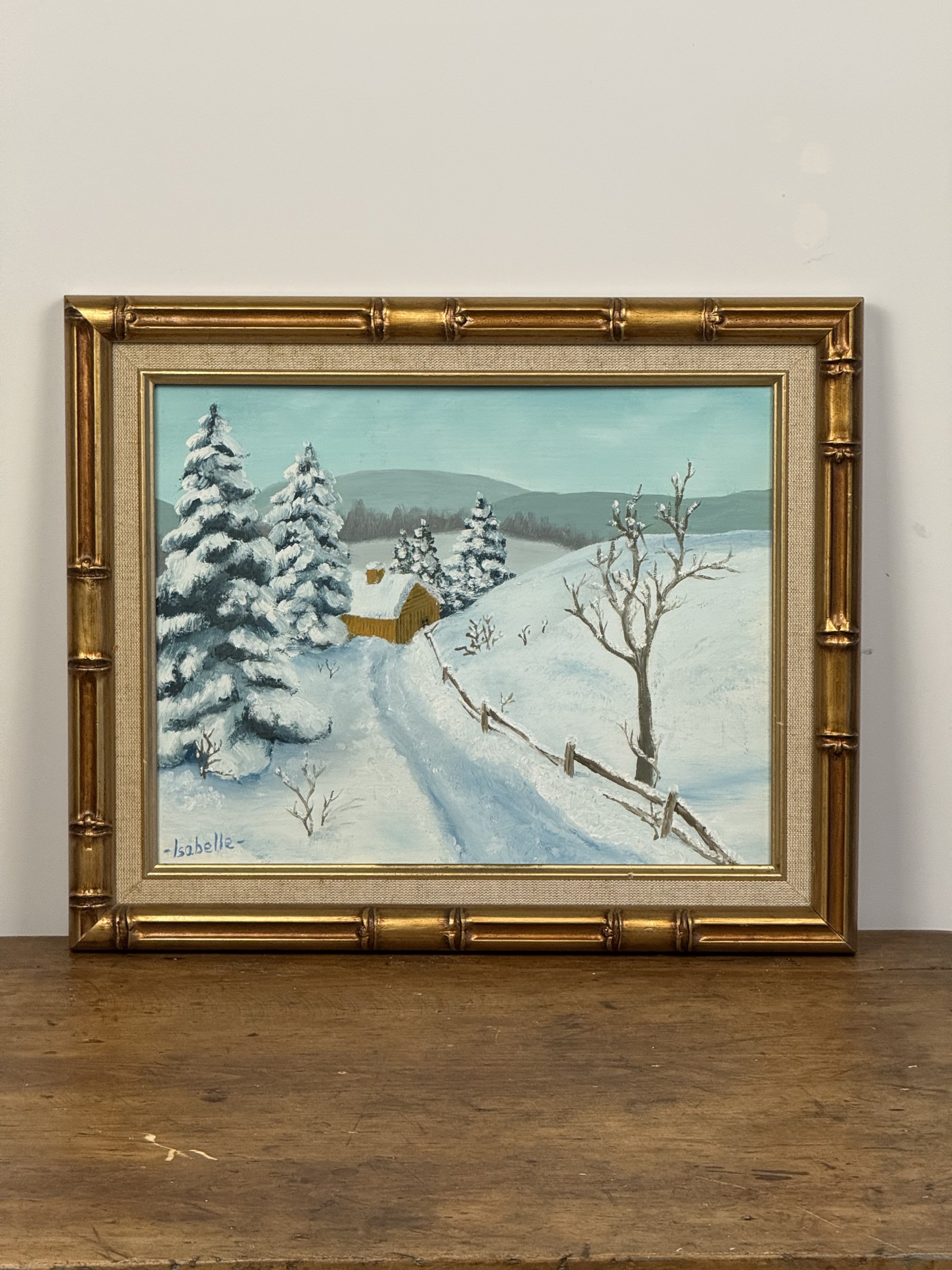 Full view of framed snowy countryside painting with trees, fence, and cabin, vintage gold bamboo-style frame