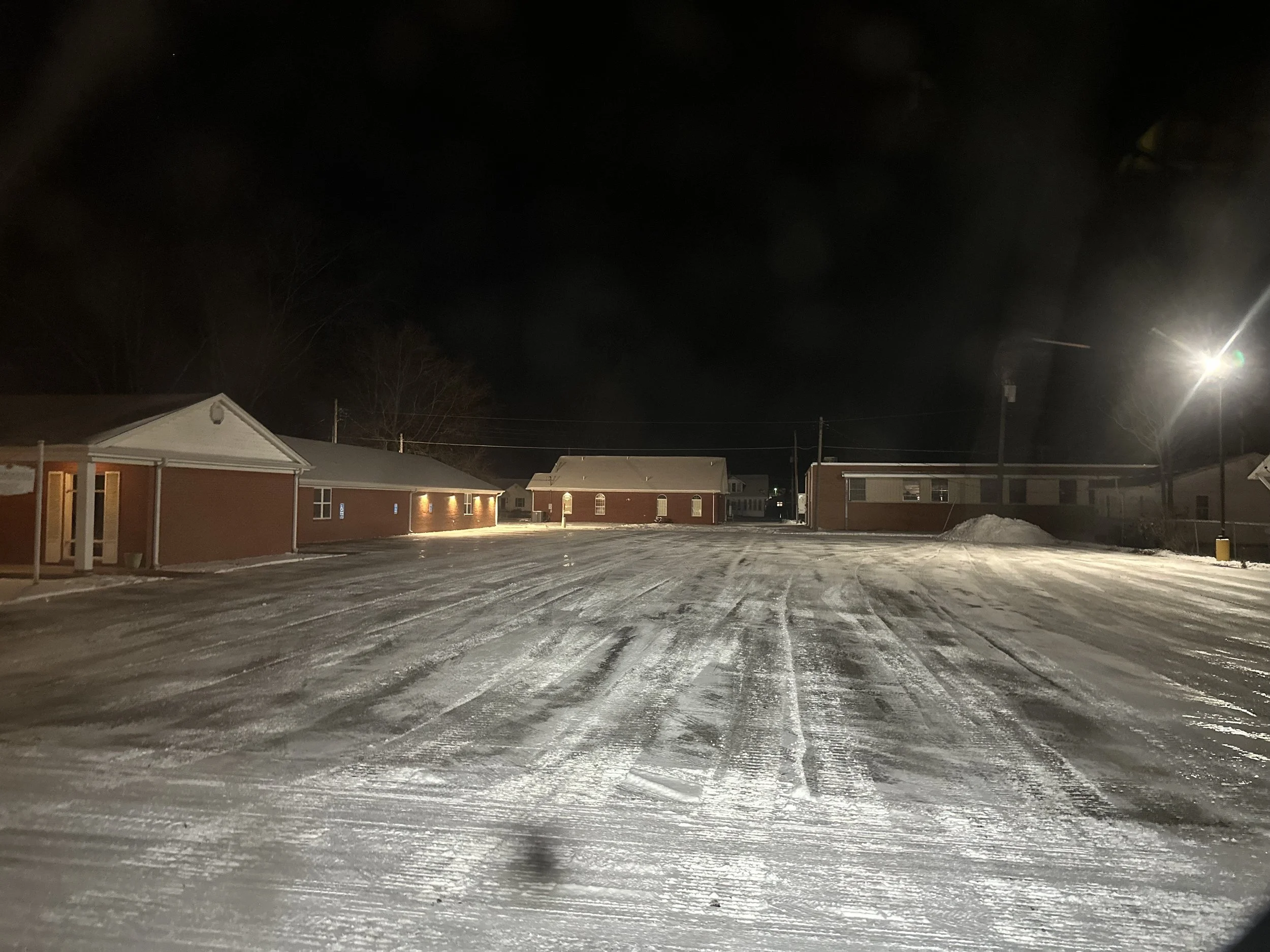 Snow-covered parking lot at night with surrounding brick buildings and streetlights.