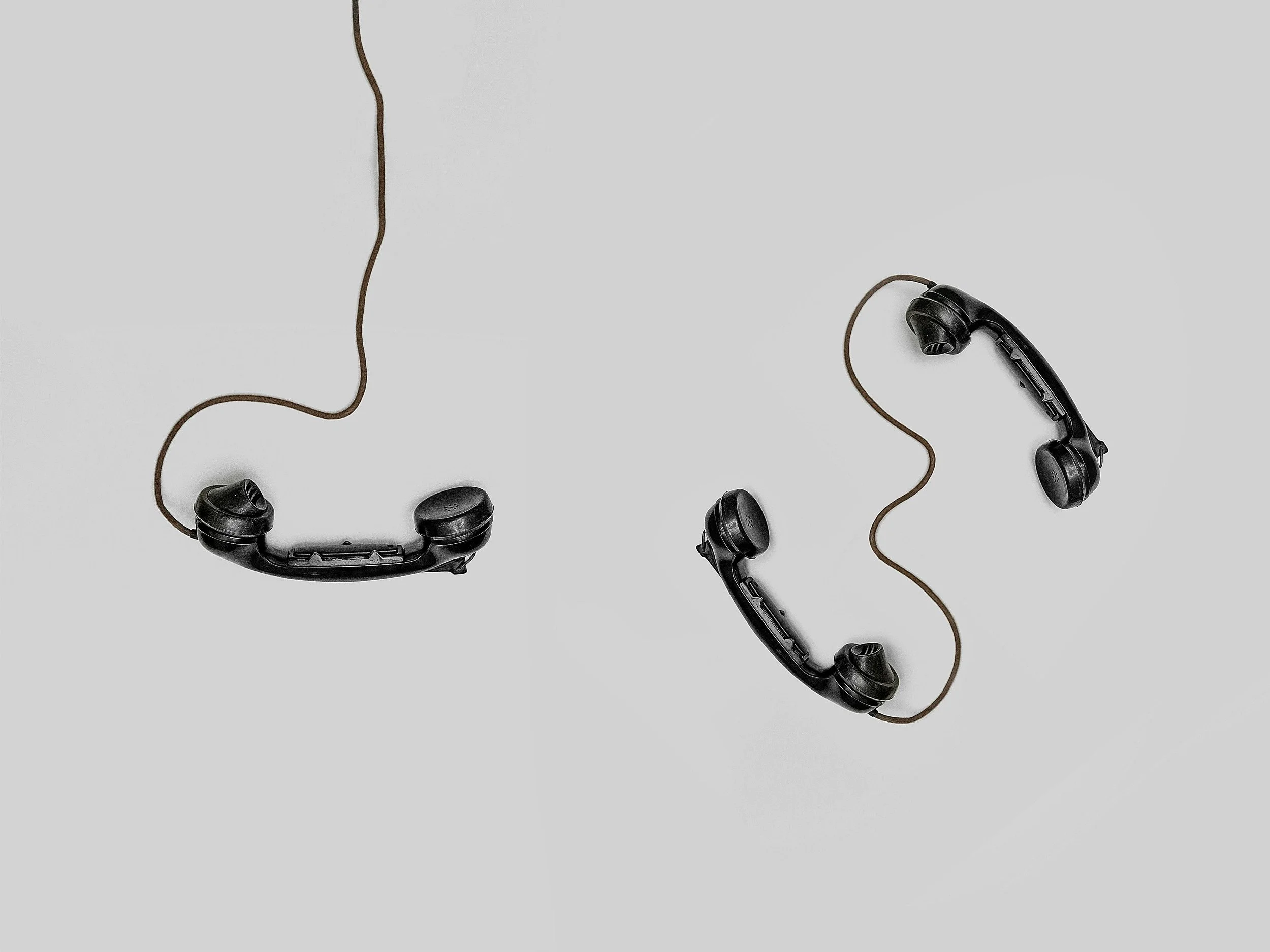 Two black vintage rotary phones with cords placed on a light grey background.