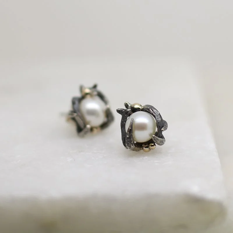 Silver and gold earrings with white pearls on a white surface.