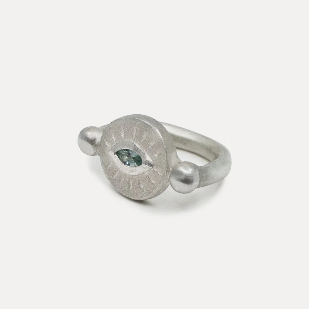 Silver ring with a circular design and a small embedded gemstone in the center on a plain white background.