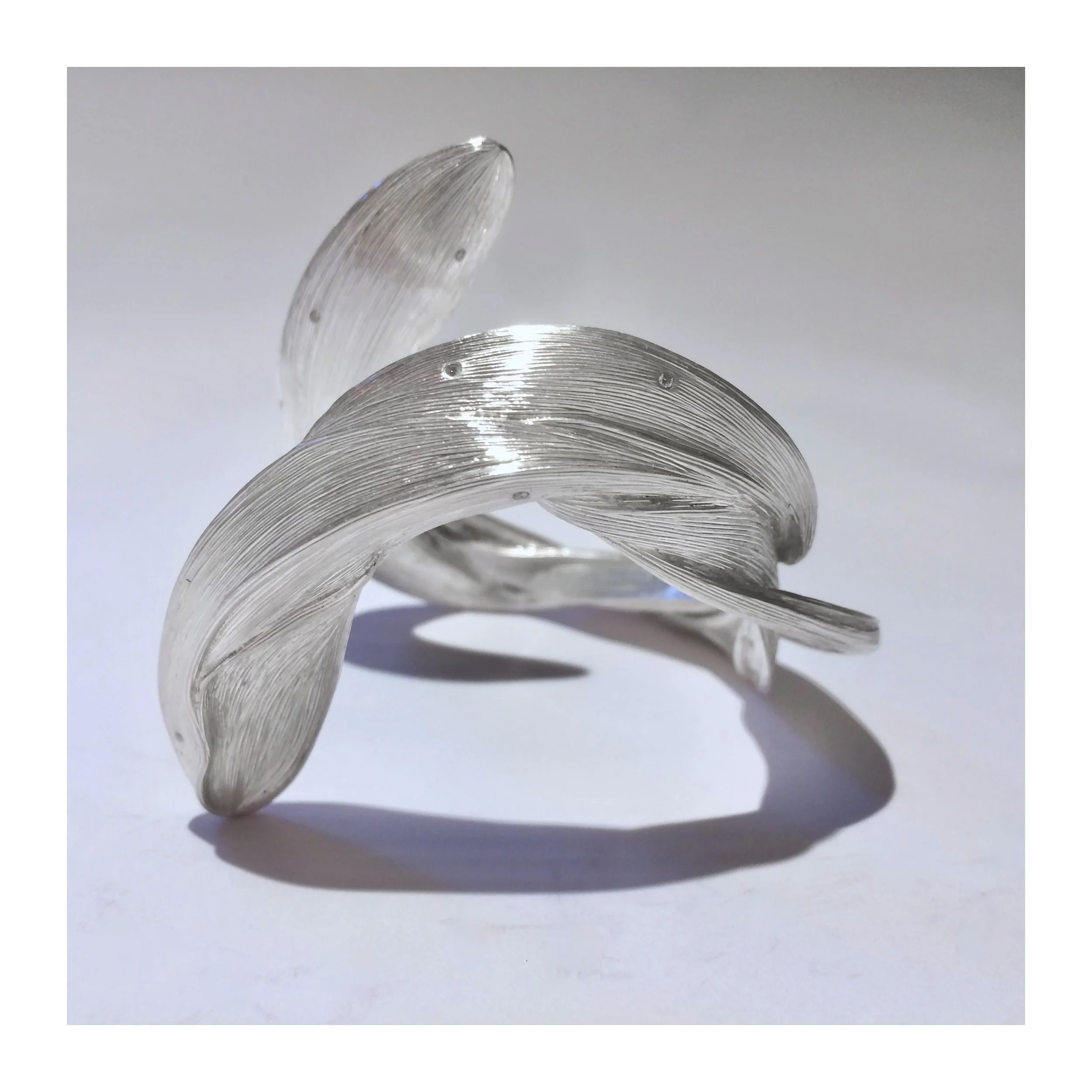 Close-up of a transparent, curved glass sculpture with textured surface, casting a shadow on a white background.