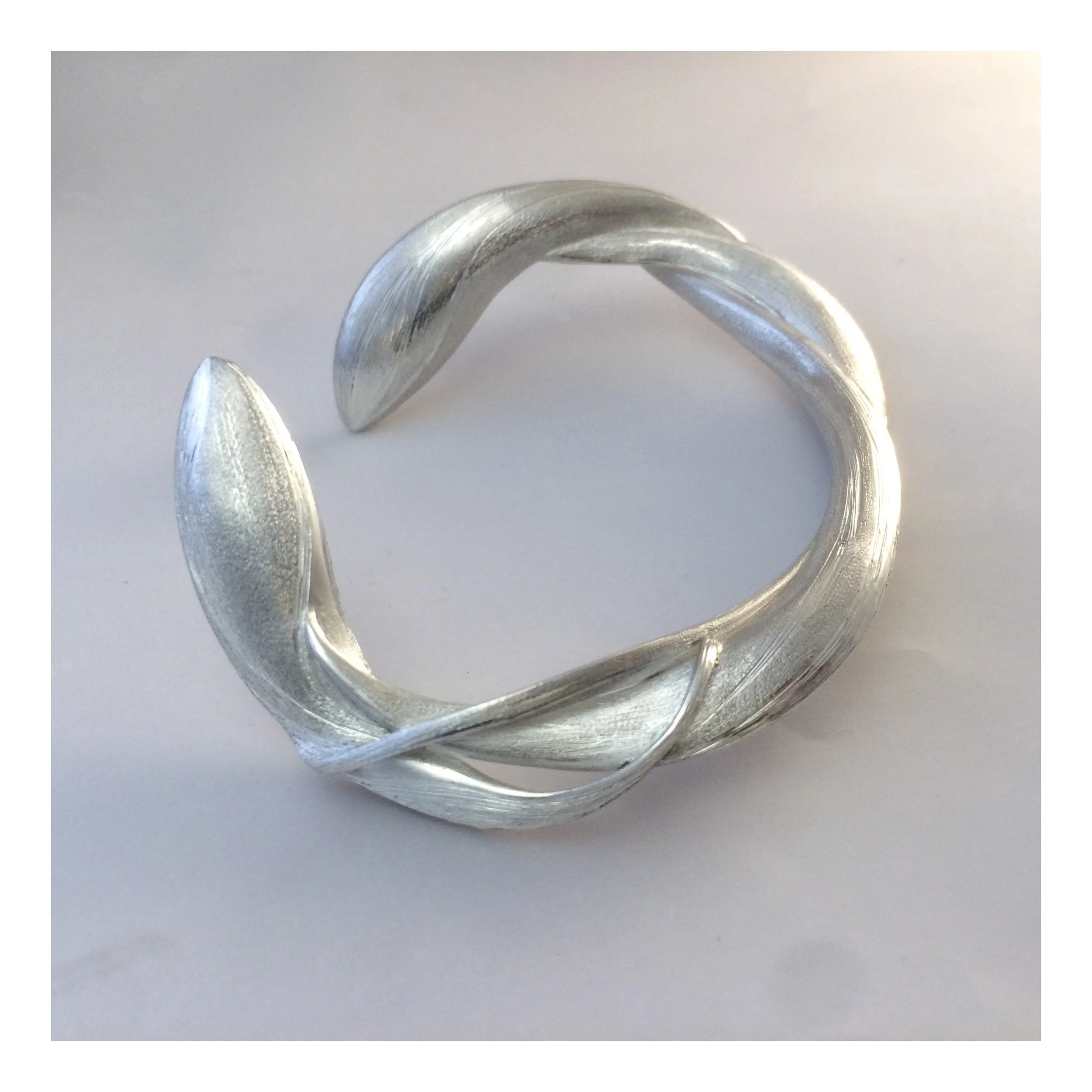 Close-up of a silver, twisted cuff bracelet with a matte finish on a white surface.