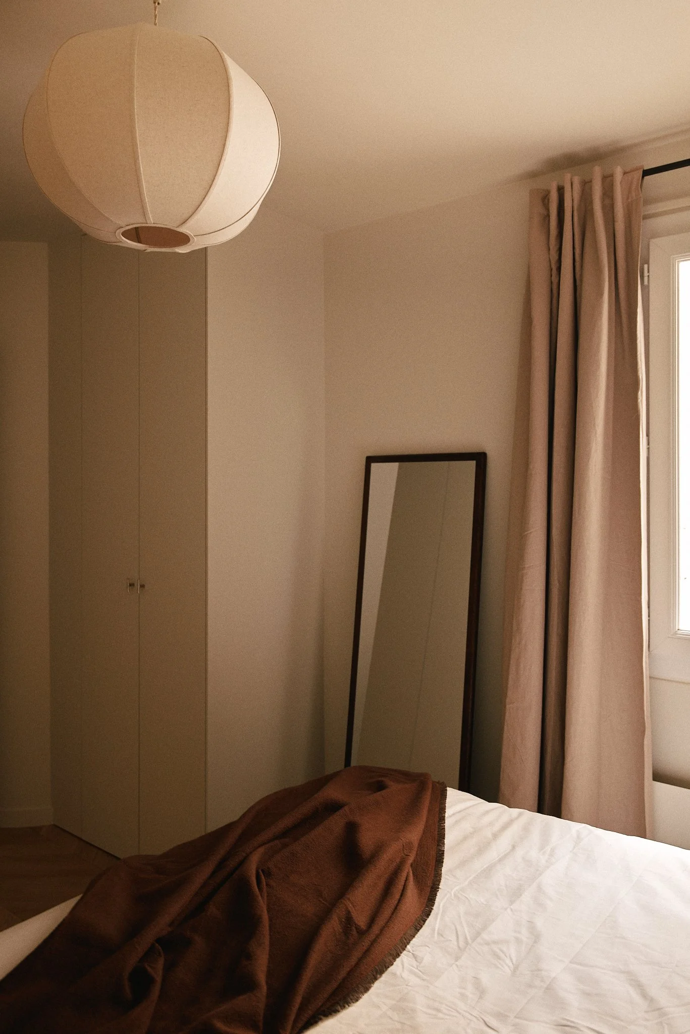Chambre avec un lit, un miroir incliné, des rideaux beige et un plafond avec un lampe suspendue