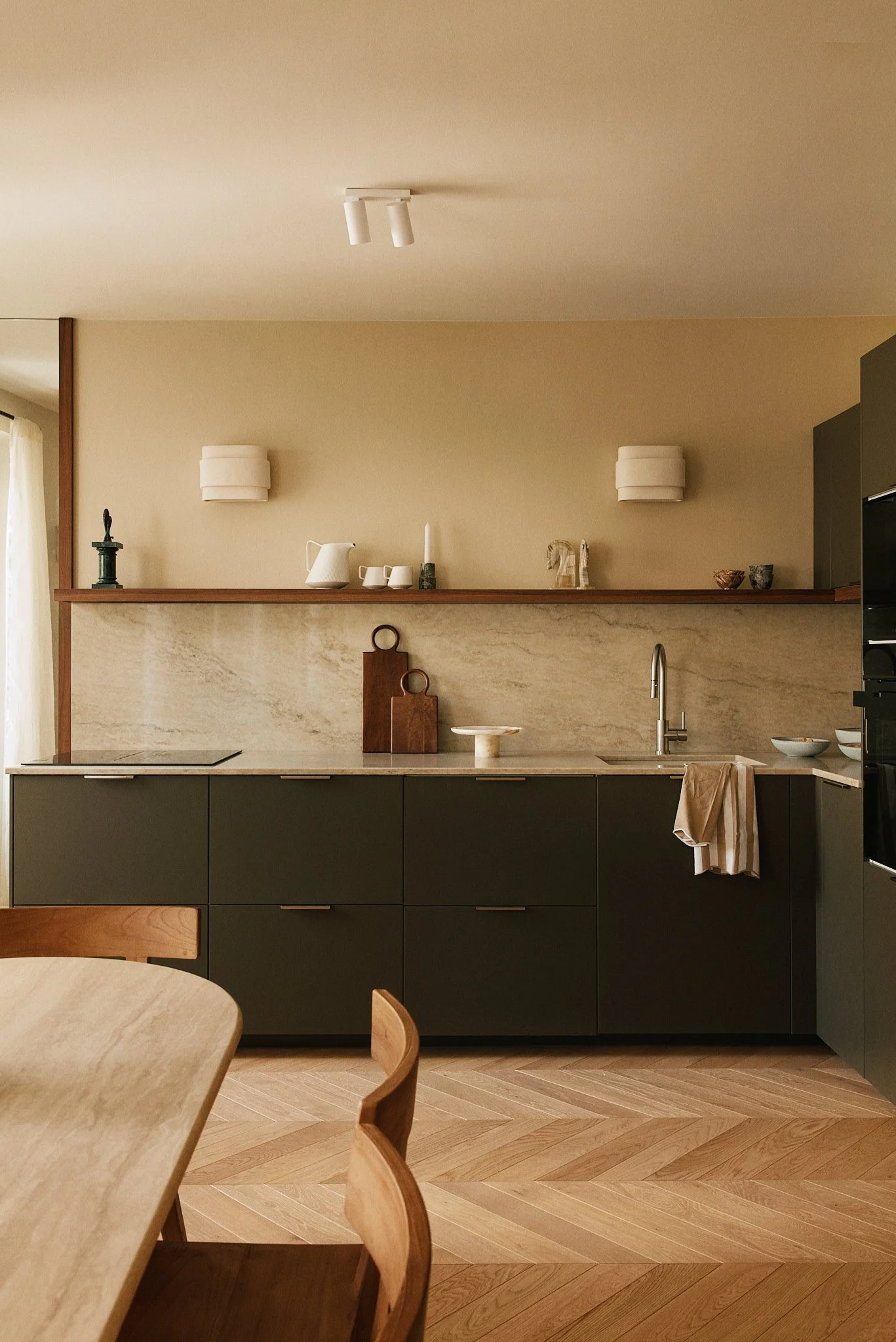 Cuisine moderne avec meubles gris foncé, plan de travail en marbre beige, décoration minimaliste avec quelques objets en porcelaine blanche, torchons en lin beige, et parquet en bois clair.