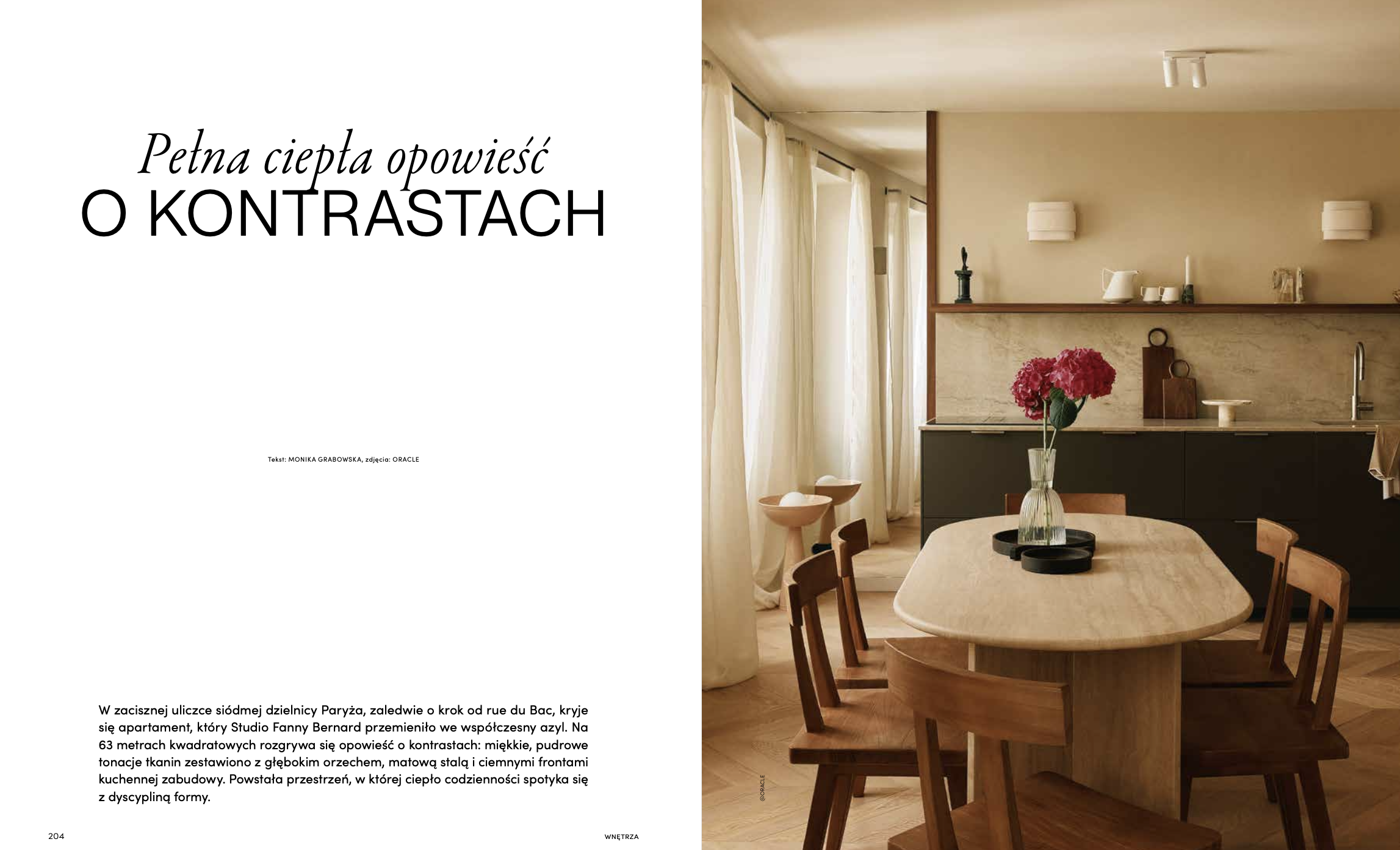 Intérieur d'une cuisine moderne avec plan de travail en pierre, armoires sombres, un vase de fleurs roses sur une table en bois clair, grande fenêtre avec rideaux clairs, décor minimaliste